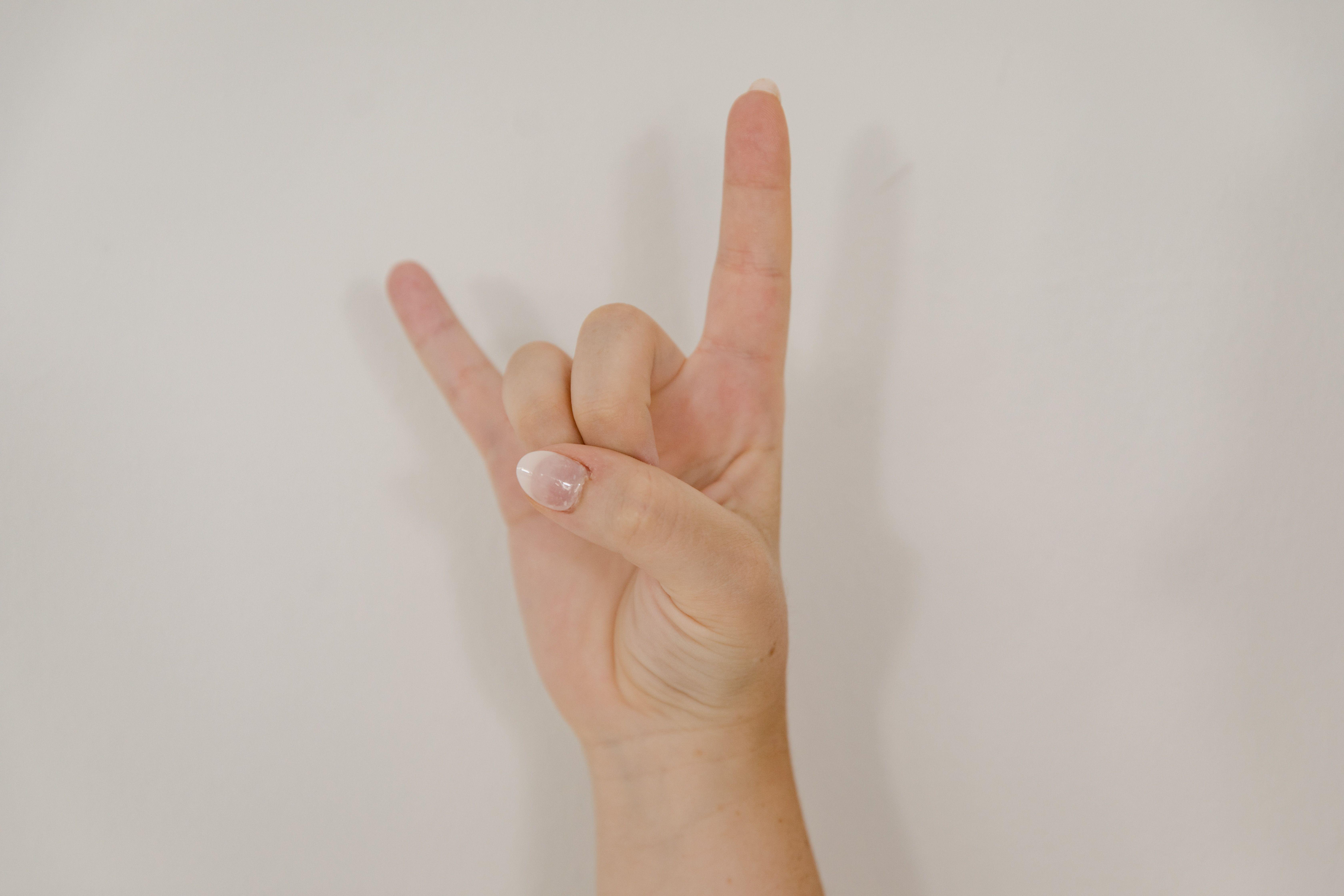 Close-up of hand making 'I Love You' gesture in American Sign Language against white background.