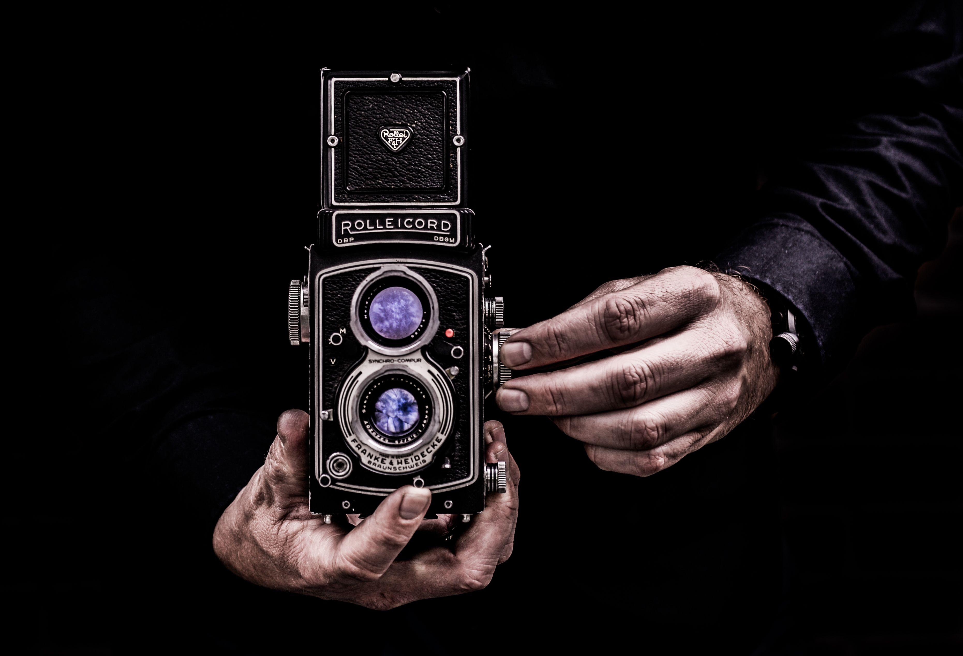 Close-up of hands holding a classic vintage Rolleicord camera against a dark background.