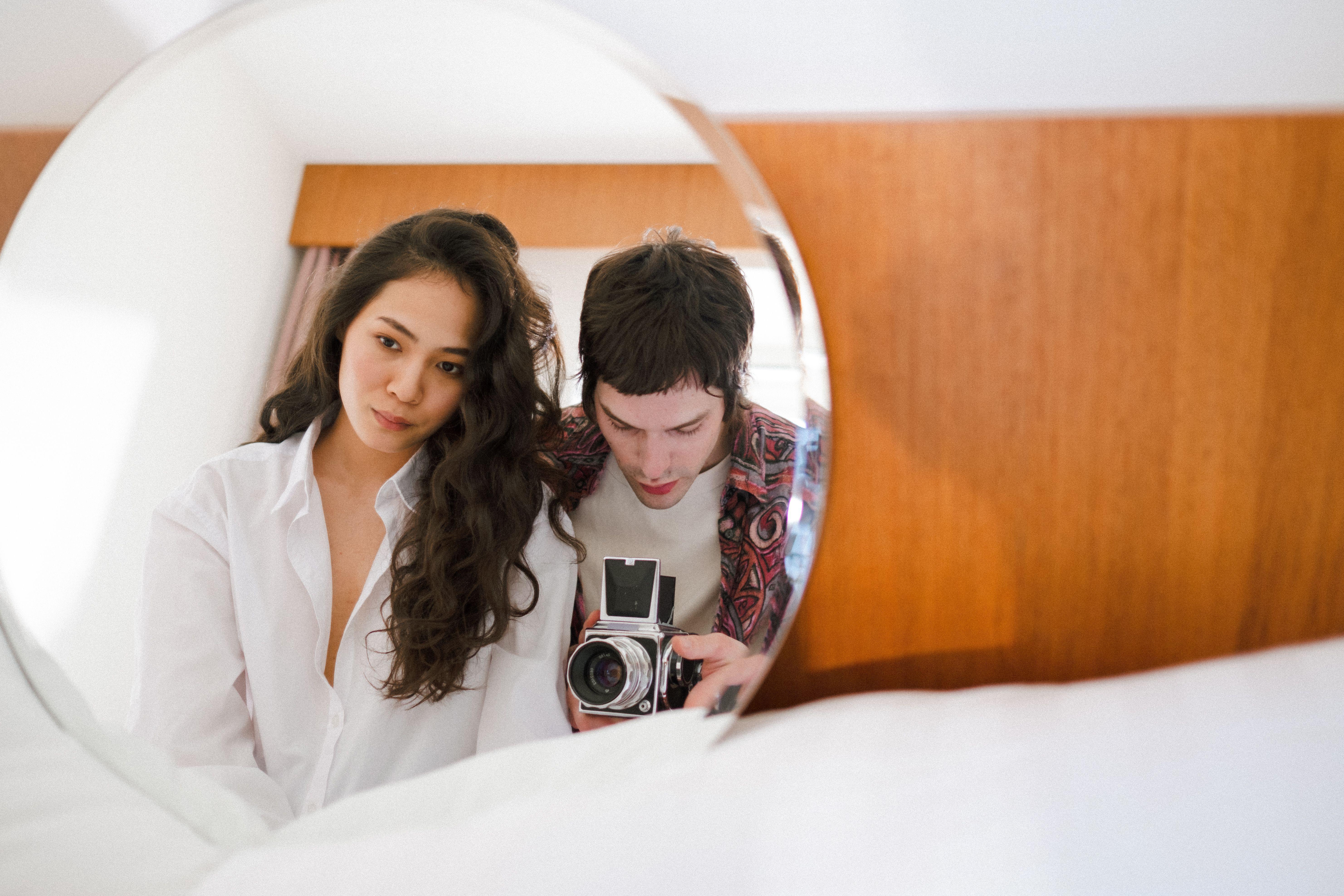 Intimate portrait of a couple using a vintage camera reflected in a mirror indoors.