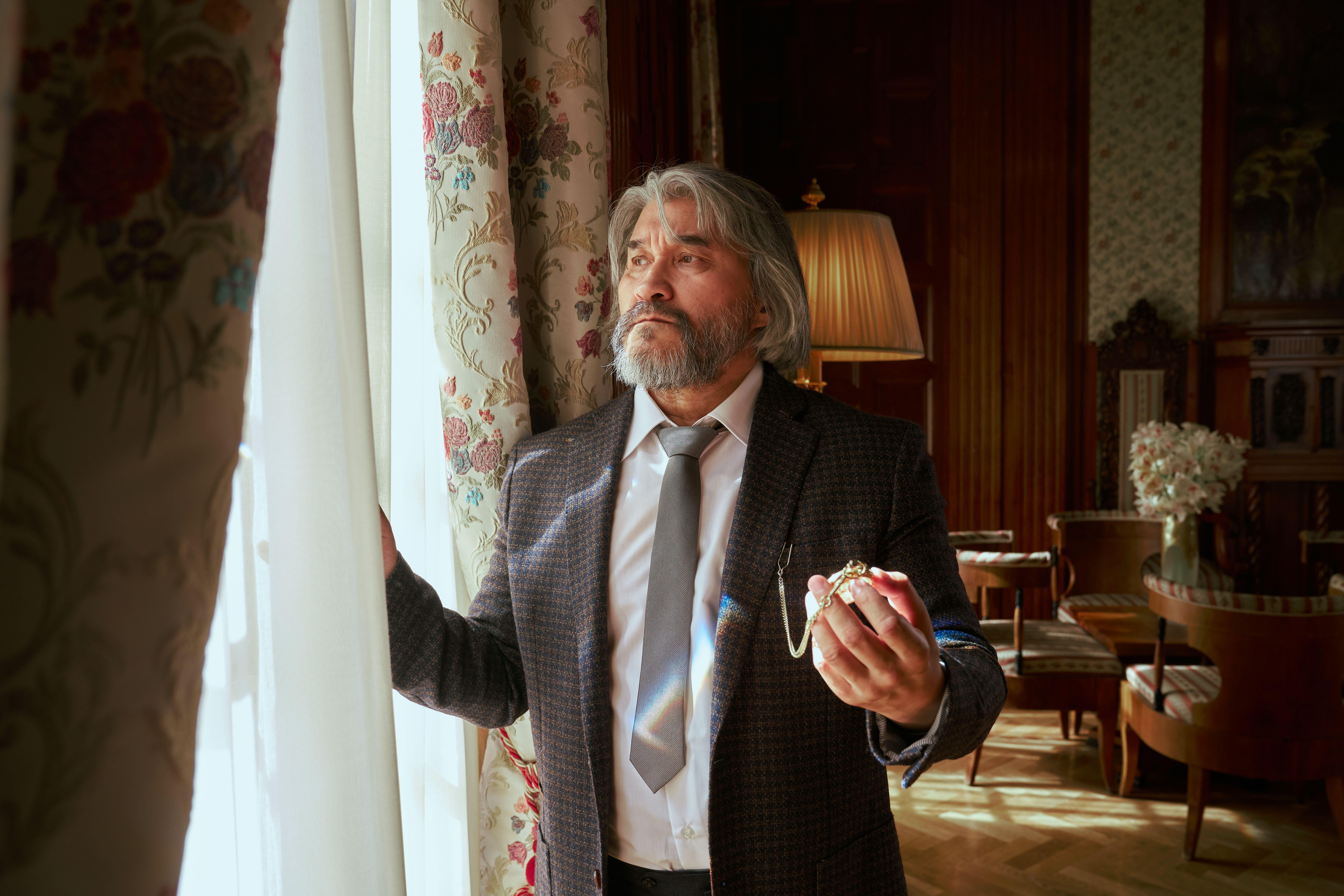 Portrait of a senior man standing by a window in an elegant, luxurious interior with a vintage touch.