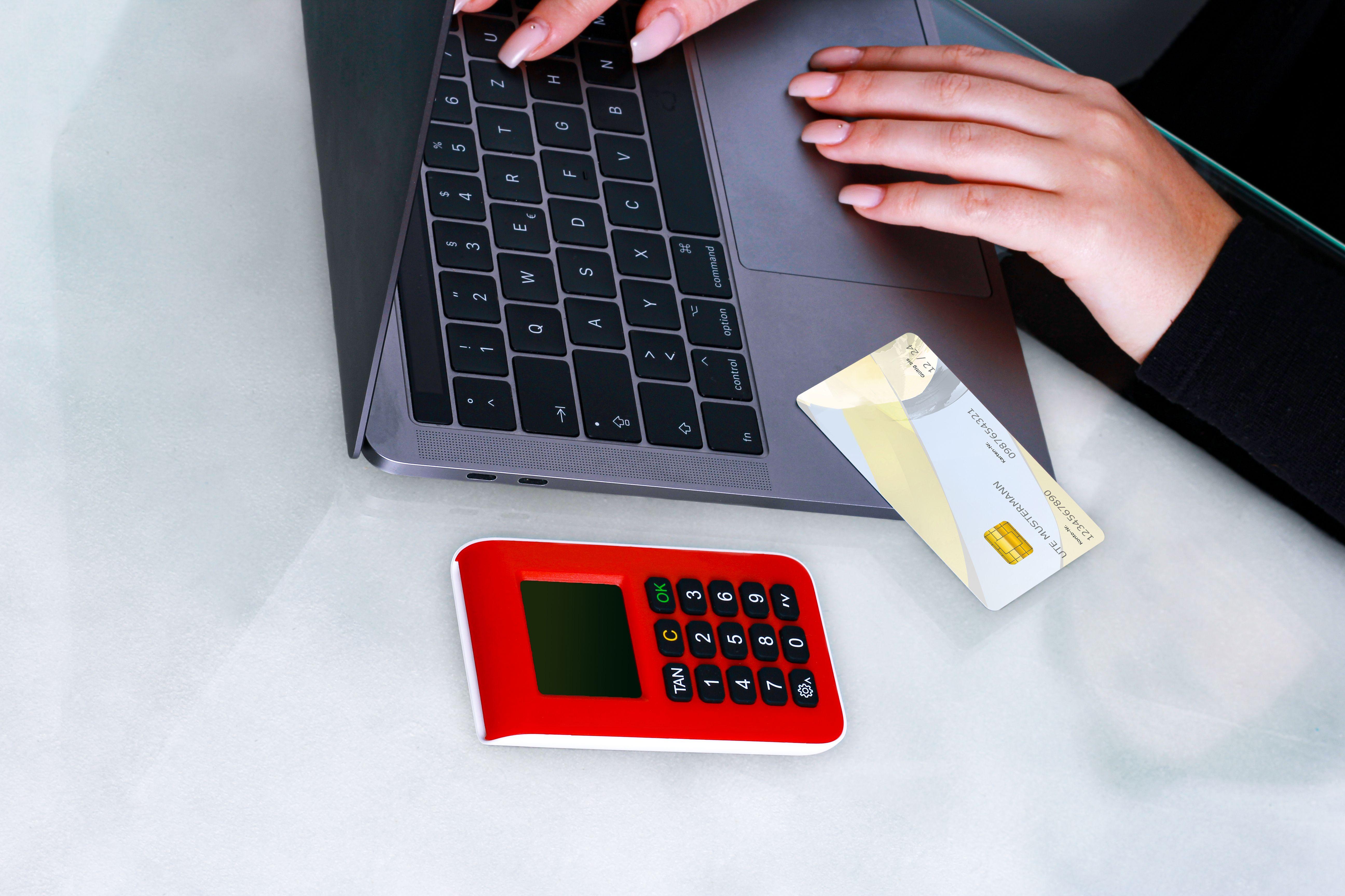 Hands using laptop with credit card and security device for online payment, emphasizing cybersecurity.