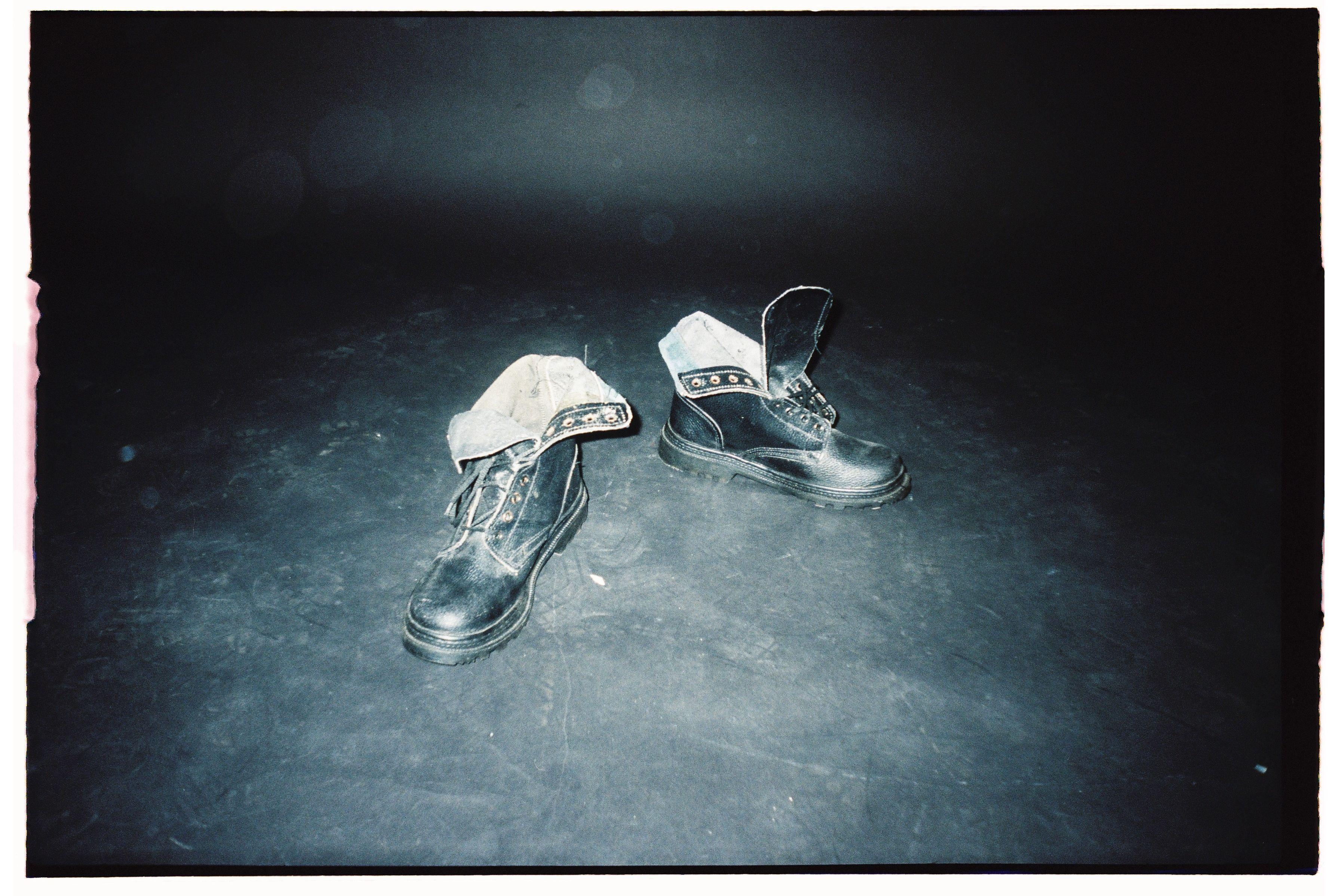 Close-up of black leather boots on a dusty floor under spotlight.