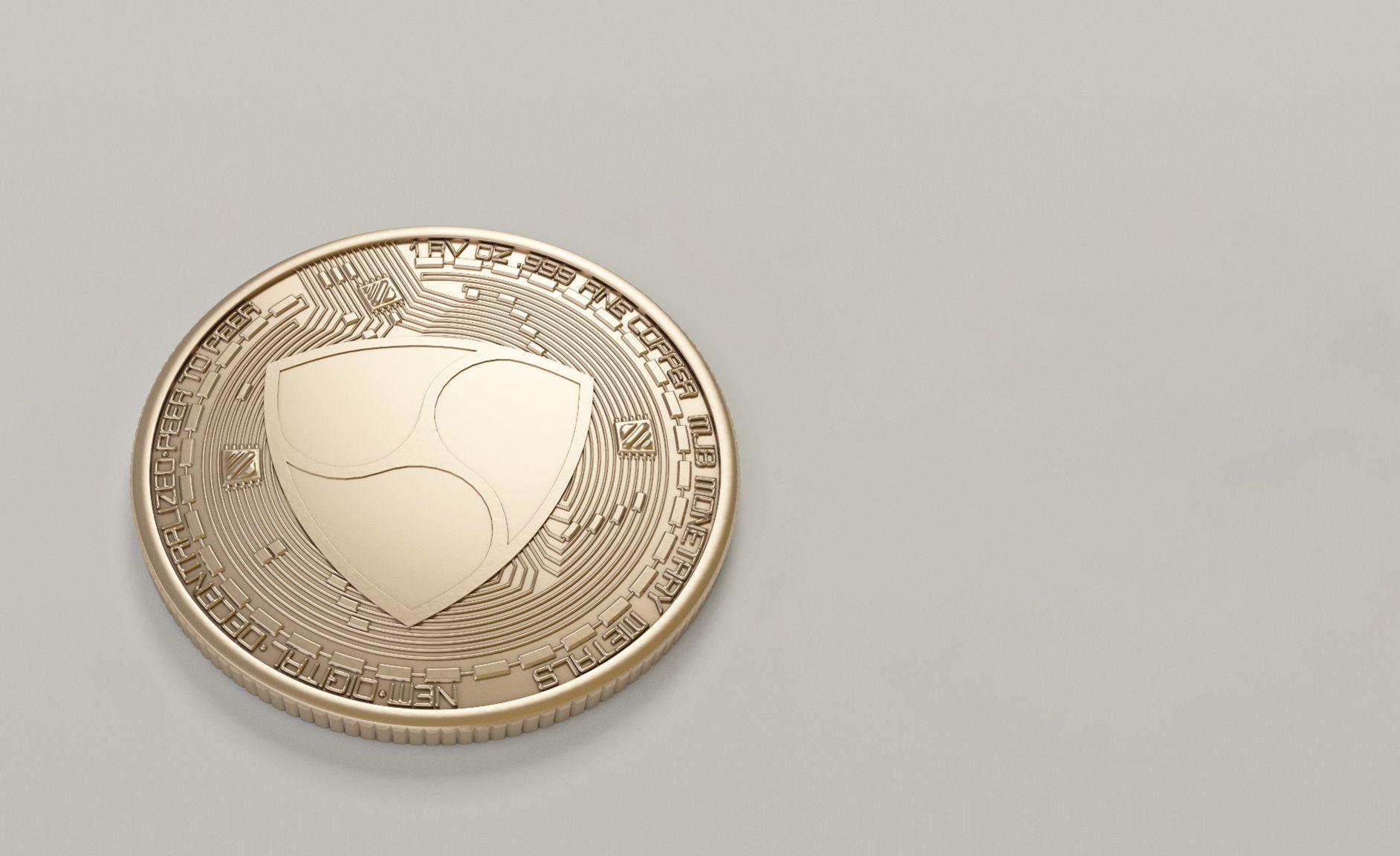 Close-up of a golden NEM cryptocurrency coin on a neutral background.