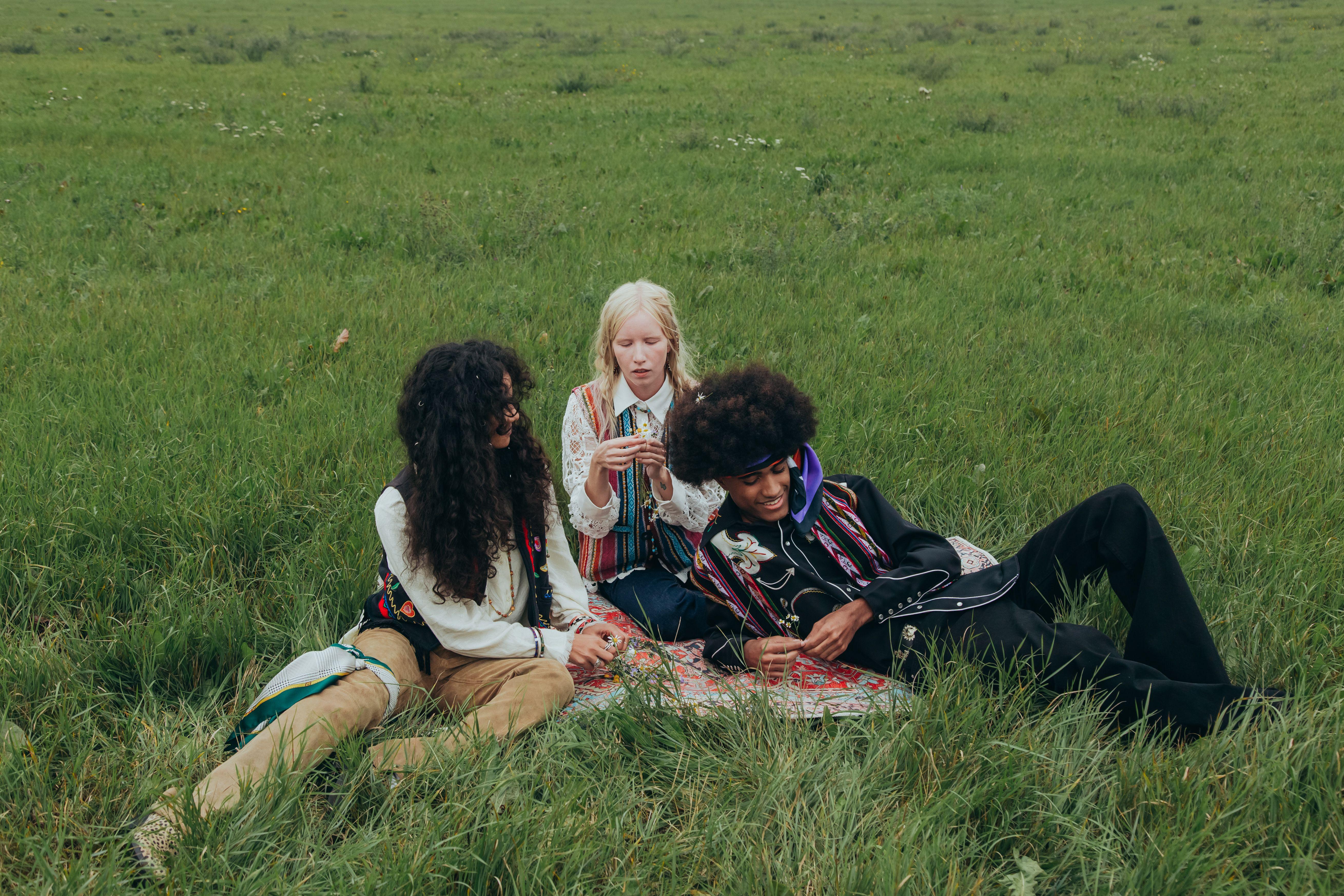 Three young adults enjoying a relaxing time on a picnic blanket in a grassy field, embracing nature and friendship.