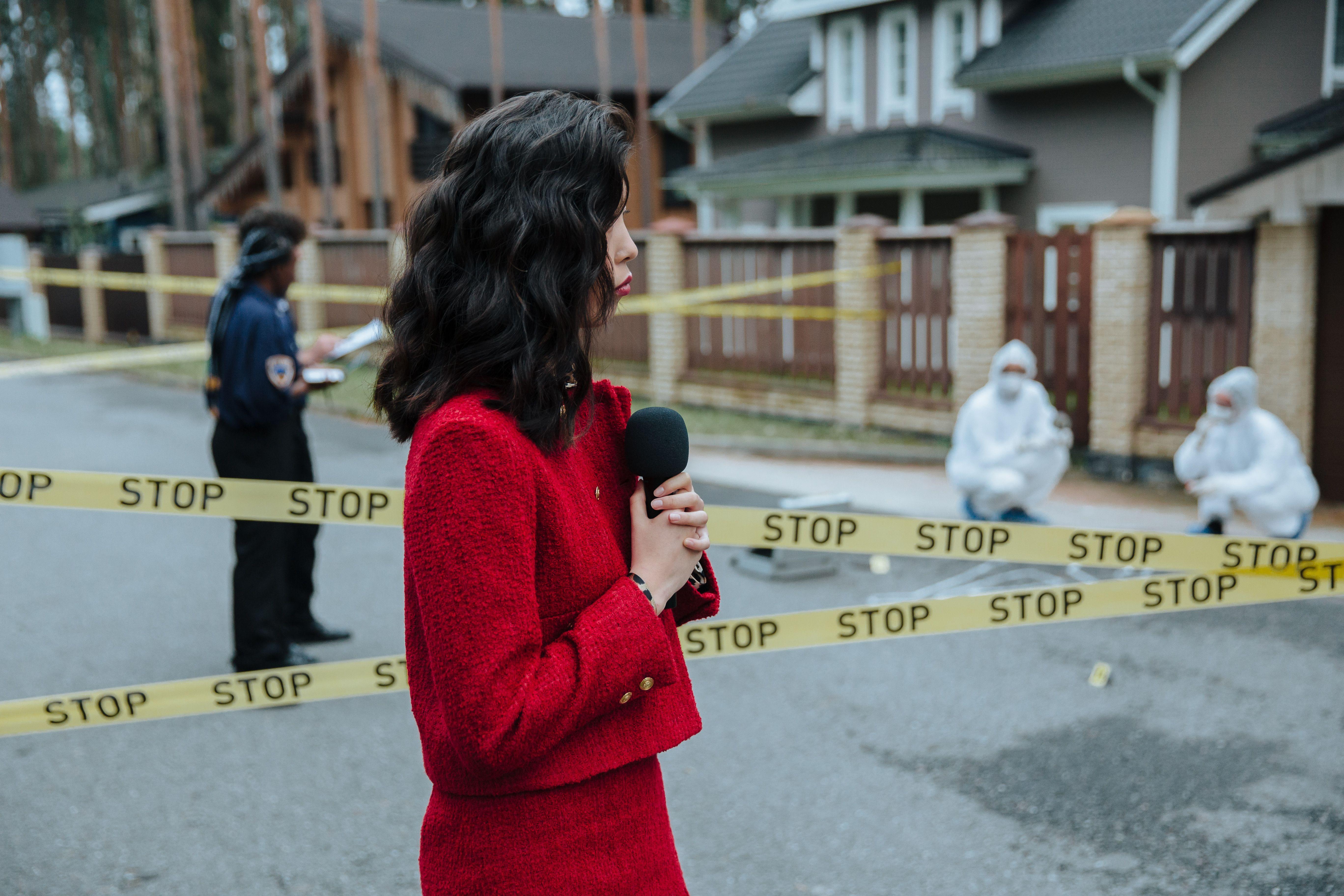 Female journalist reporting live on a crime scene investigation with police presence outdoors.