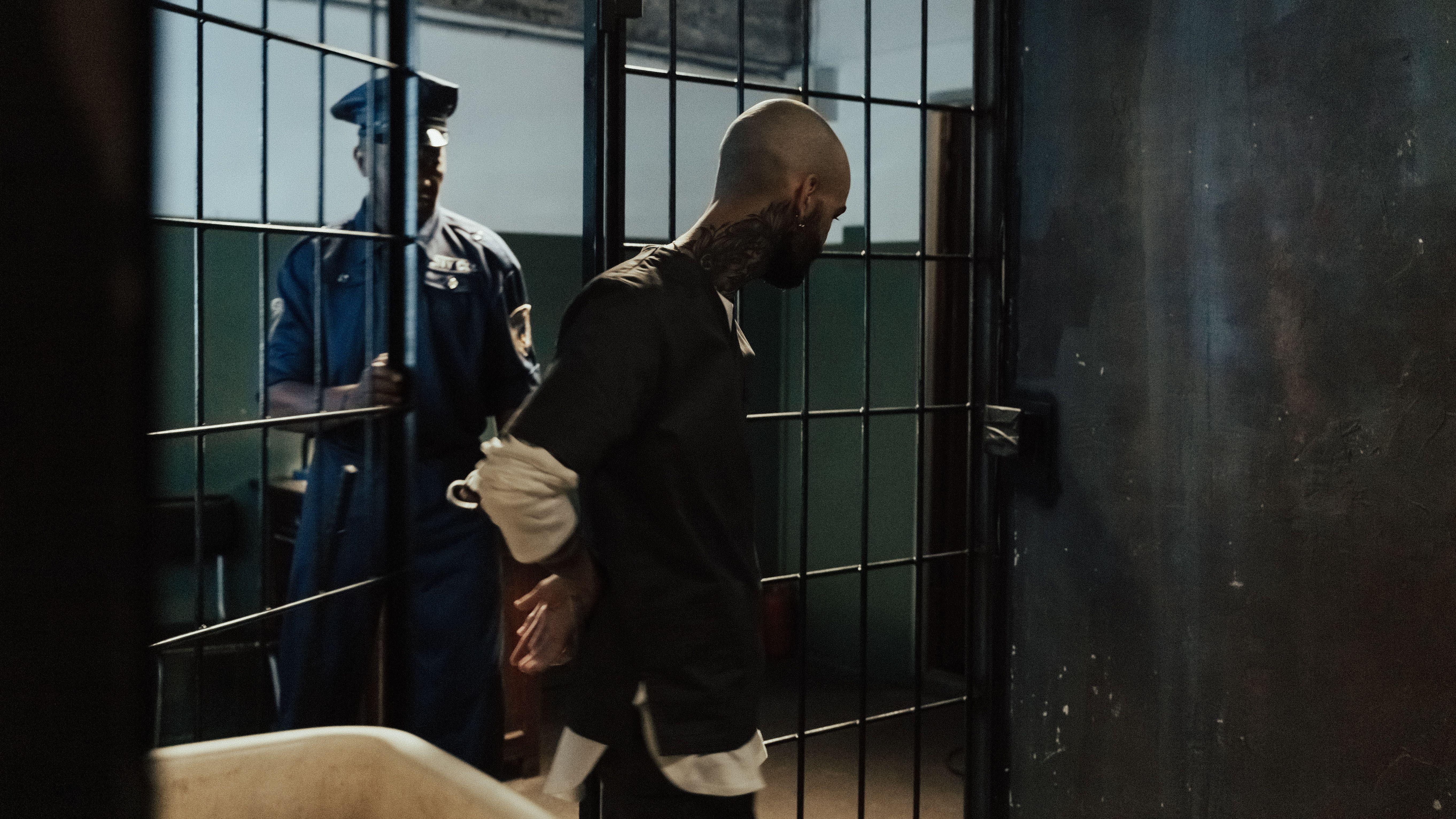 Police officer escorting a handcuffed prisoner through a dimly lit jail corridor.