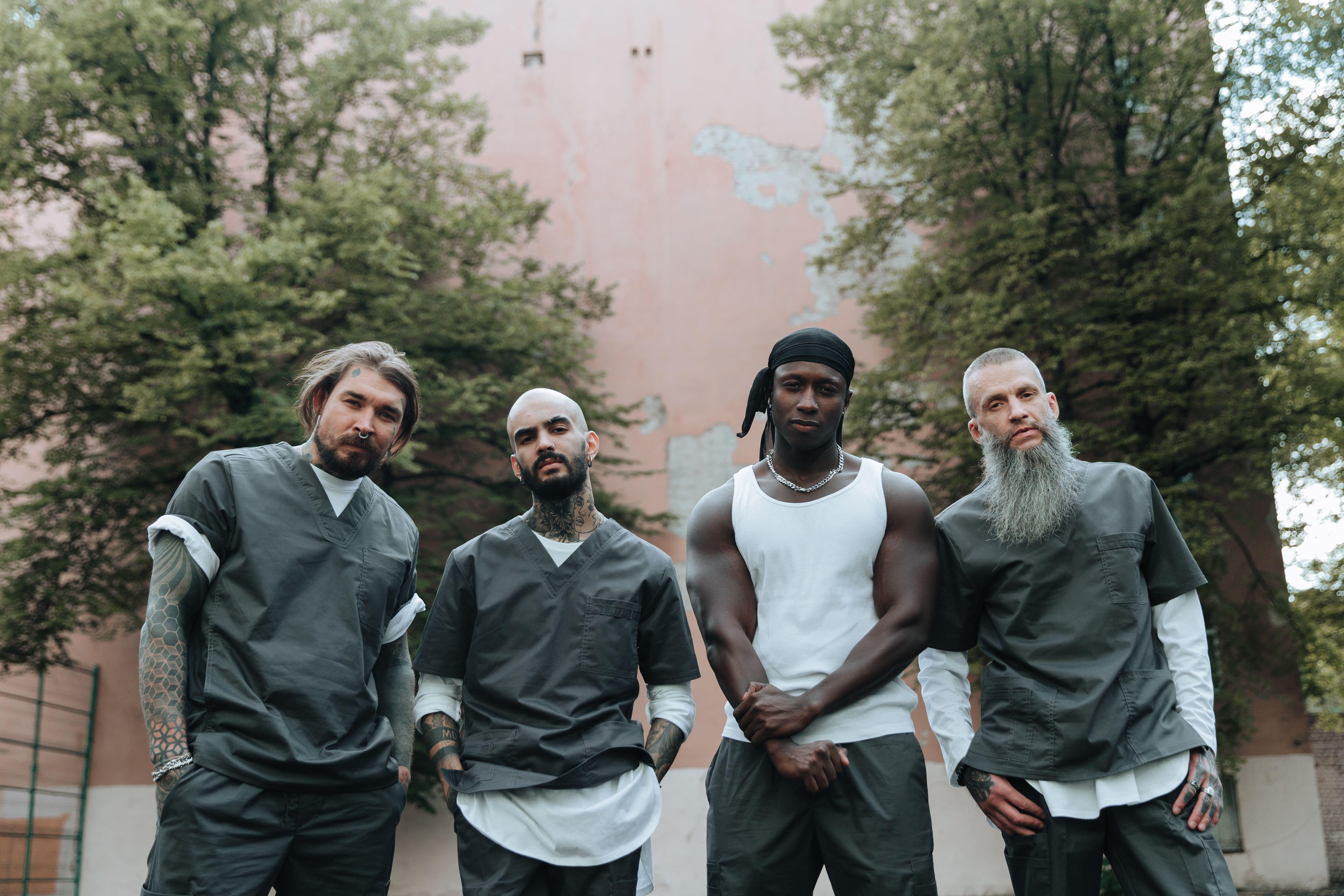 Four men in prison attire standing outdoors with a serious expression.