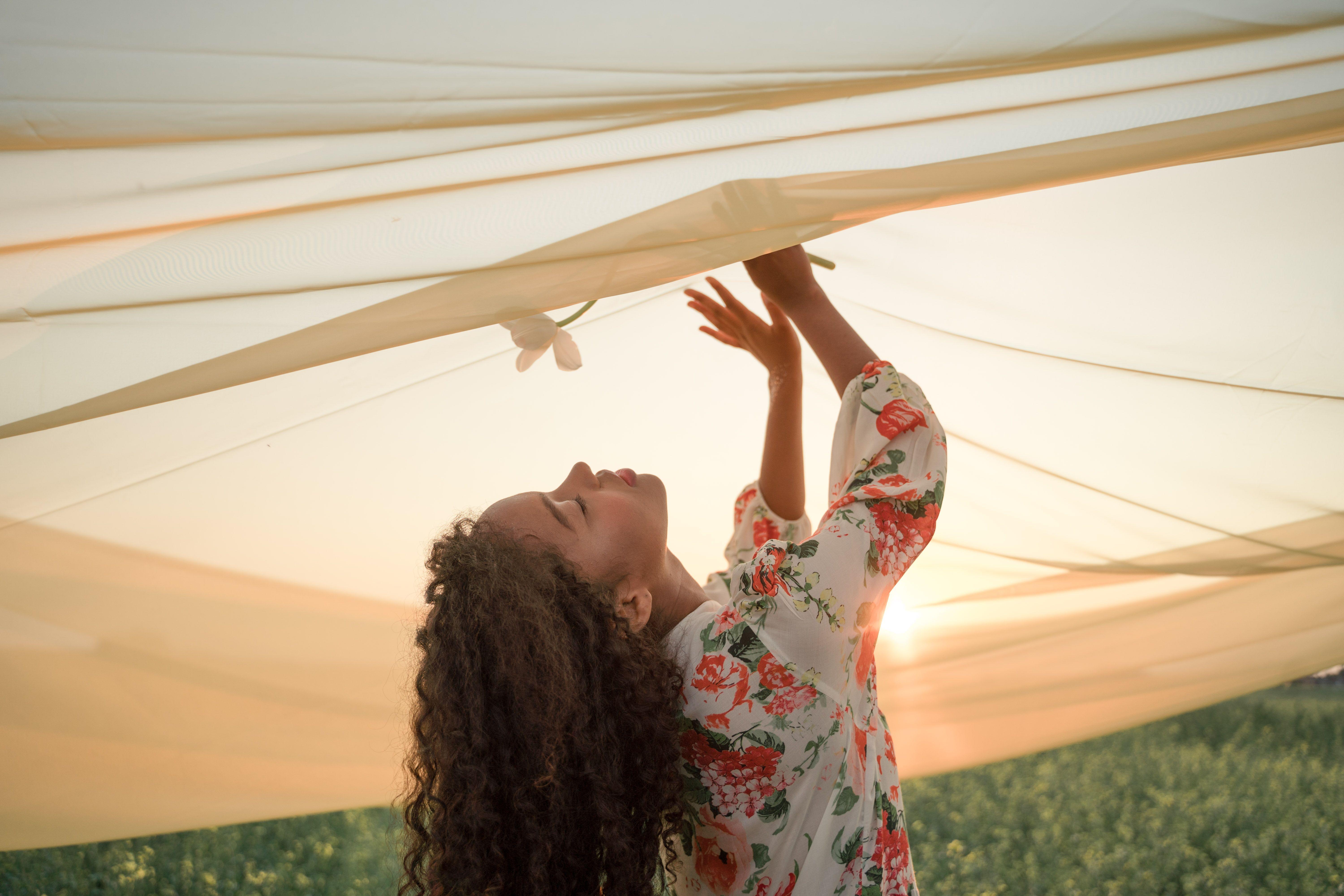 A serene woman enjoying the sunset's warm glow under flowing fabric in nature.
