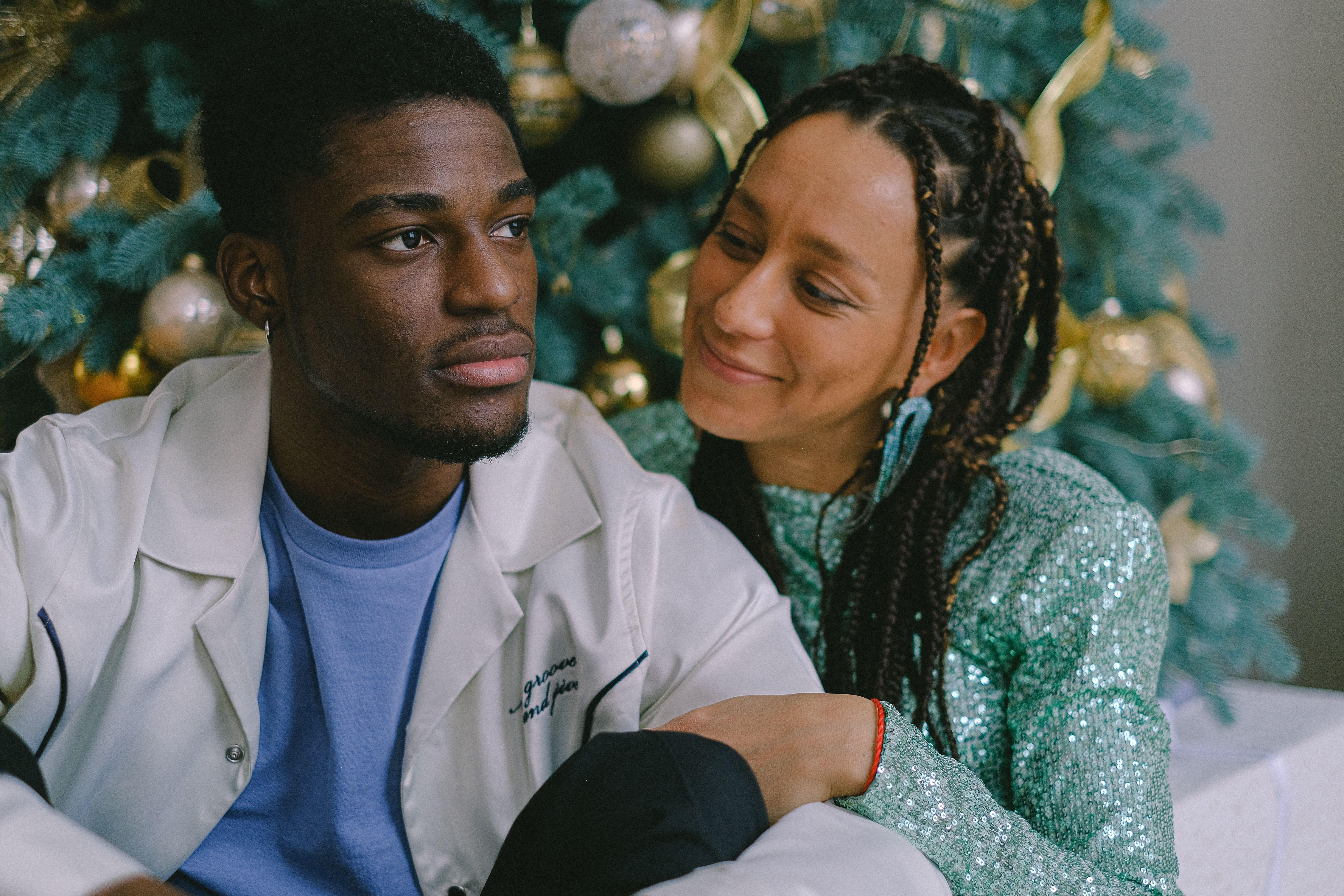 A loving couple enjoys holiday time by the decorated Christmas tree indoors.