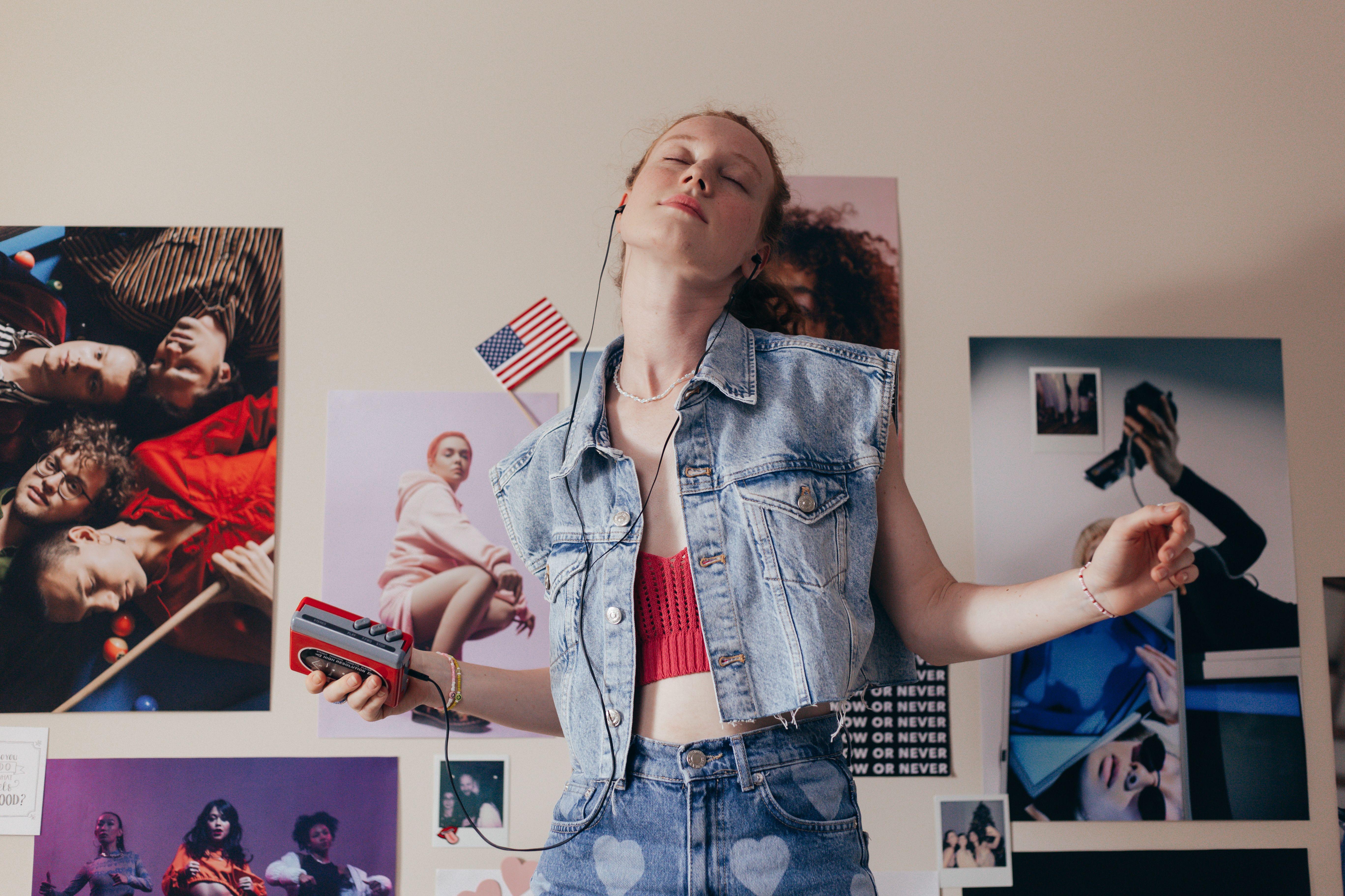 A young woman in denim enjoying music in her bedroom, embracing a retro style with a walkman and vibrant posters.
