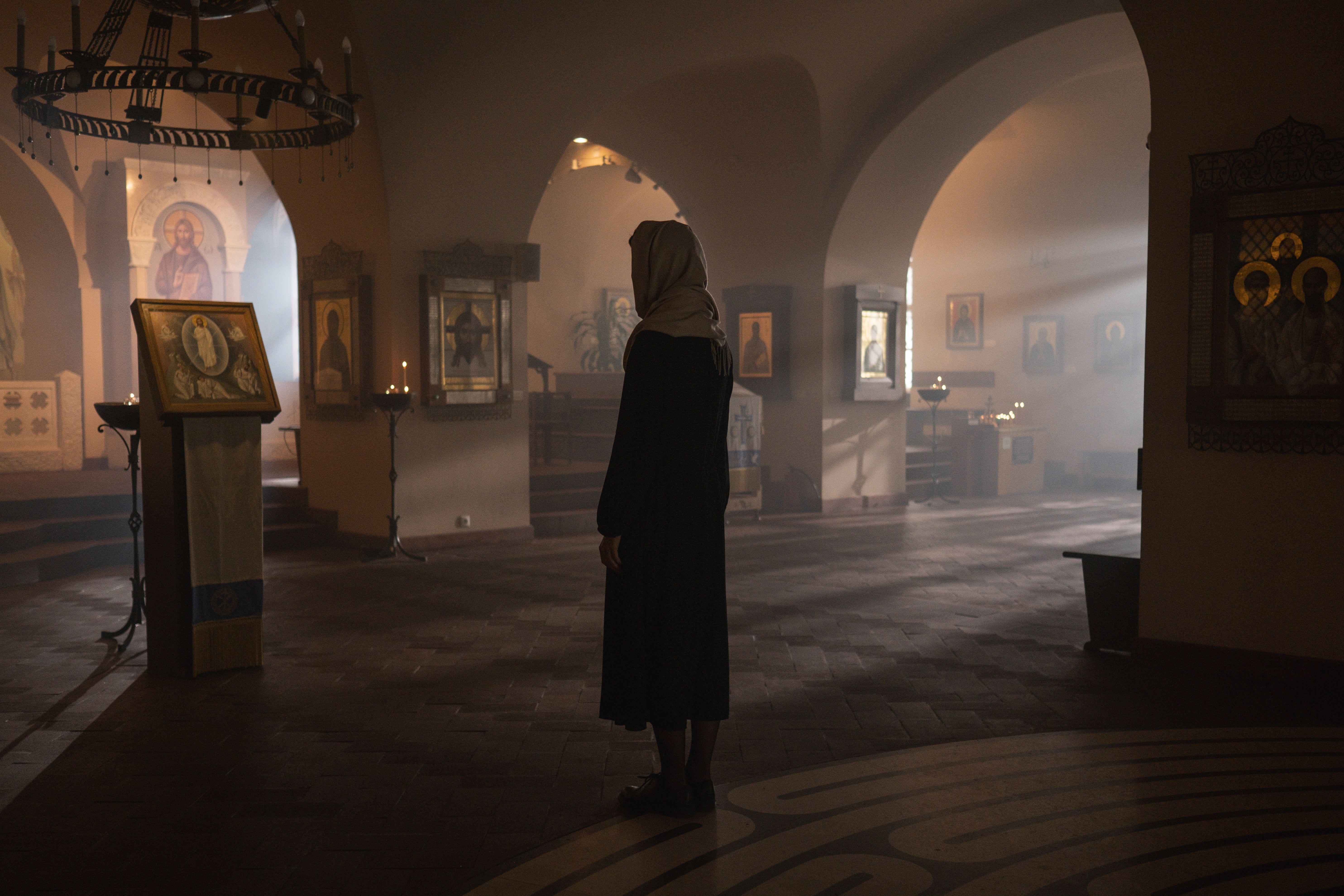 A contemplative scene inside a church with a woman standing among religious icons.