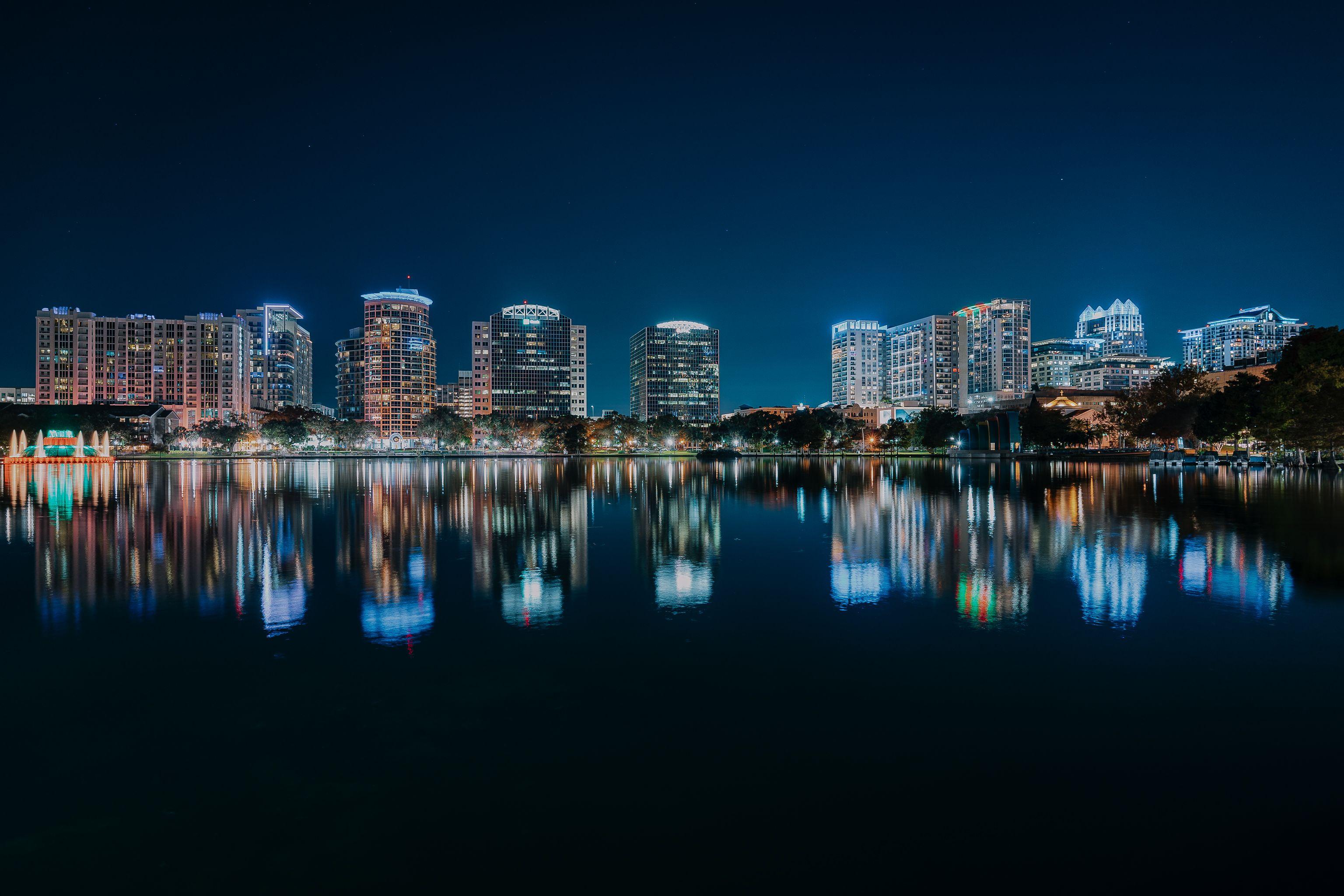 Stunning nighttime view of Orlando's illuminated skyline reflecting in a calm body of water.