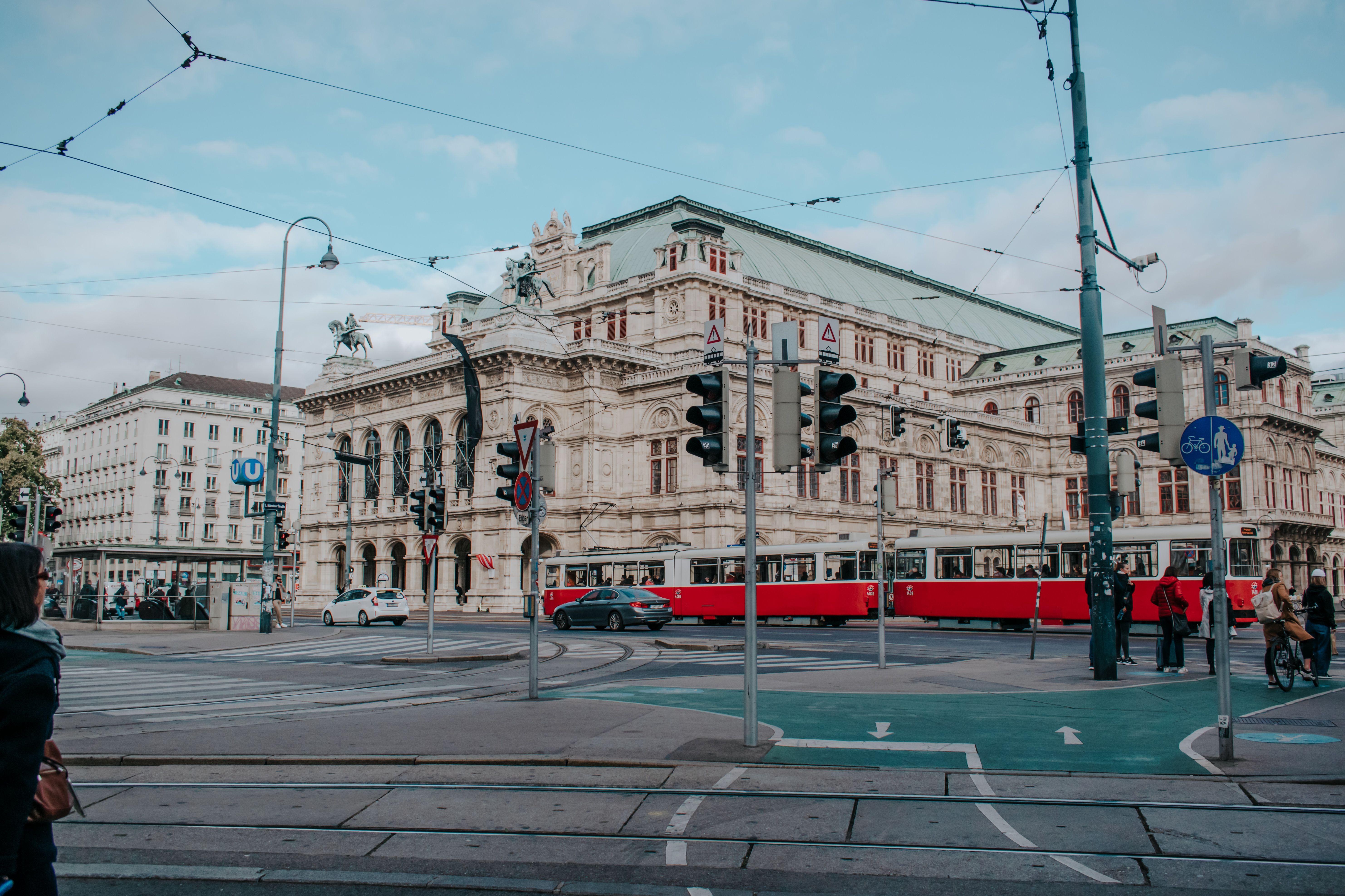 Elegant Vienna State Opera with red tram passing by, capturing the essence of Vienna's historic charm and modern city life.