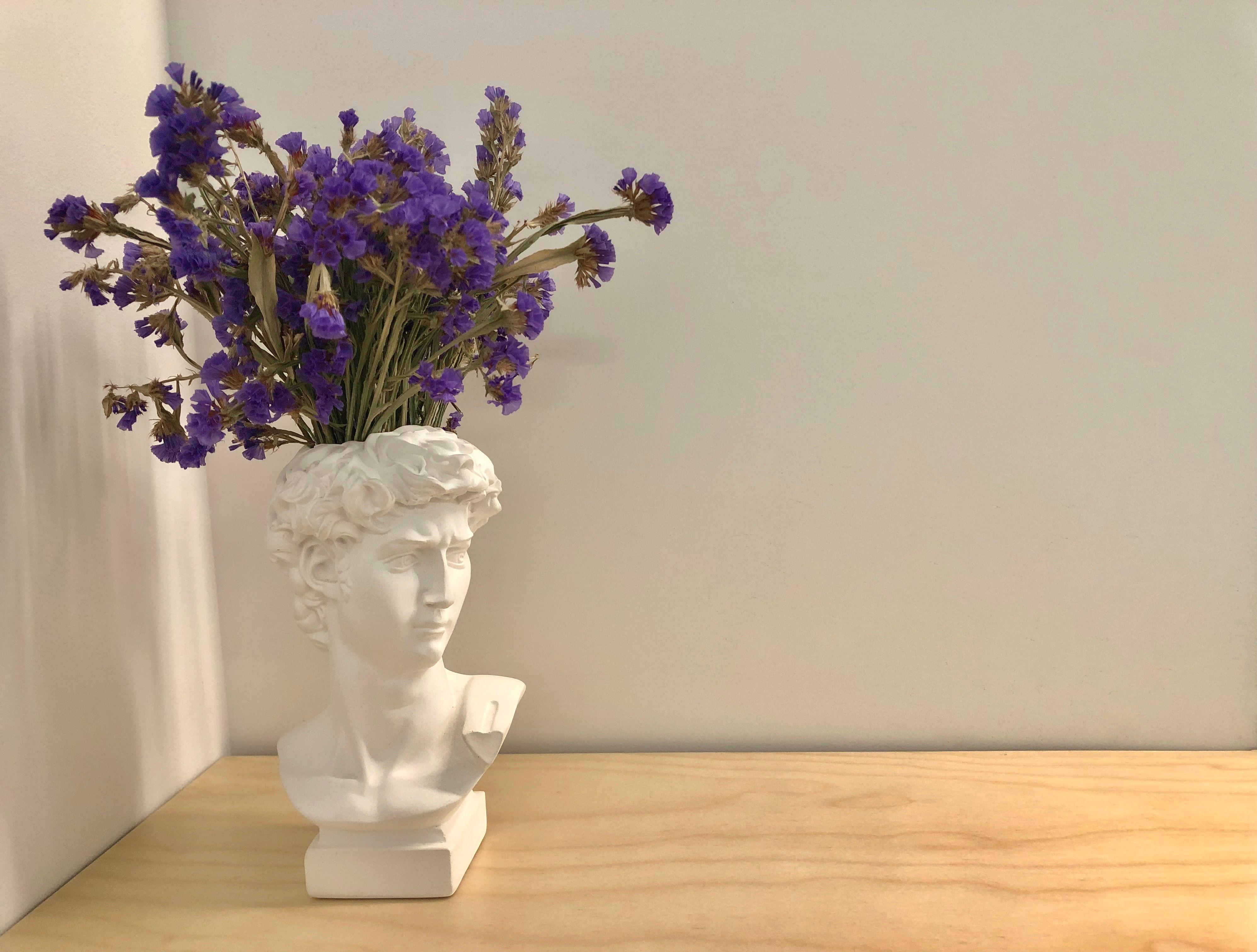 A decorative bust vase with purple flowers on a wooden table, minimalist design.