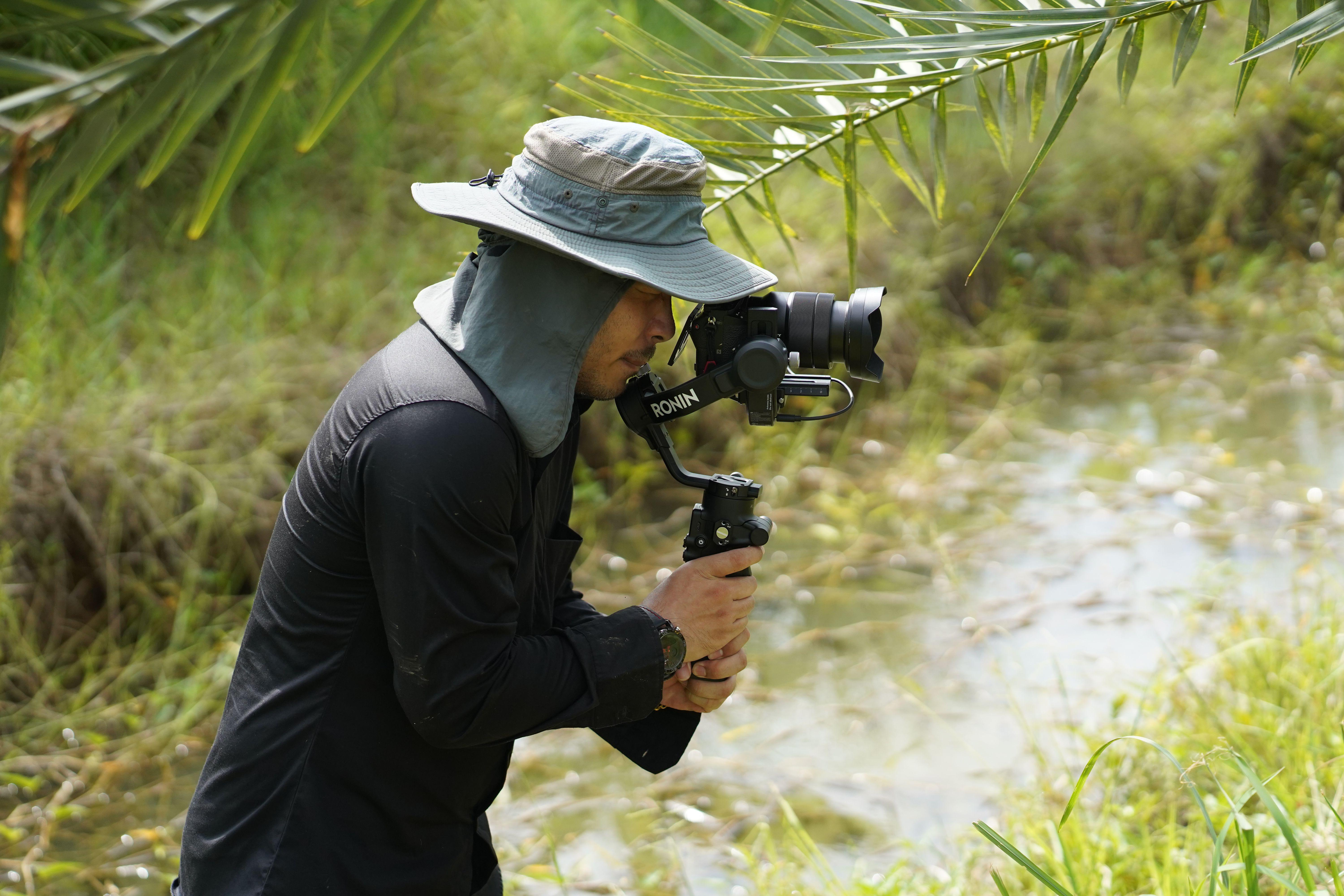 Videographer with a gimbal capturing nature scenes in lush surroundings, Buriram, Thailand.