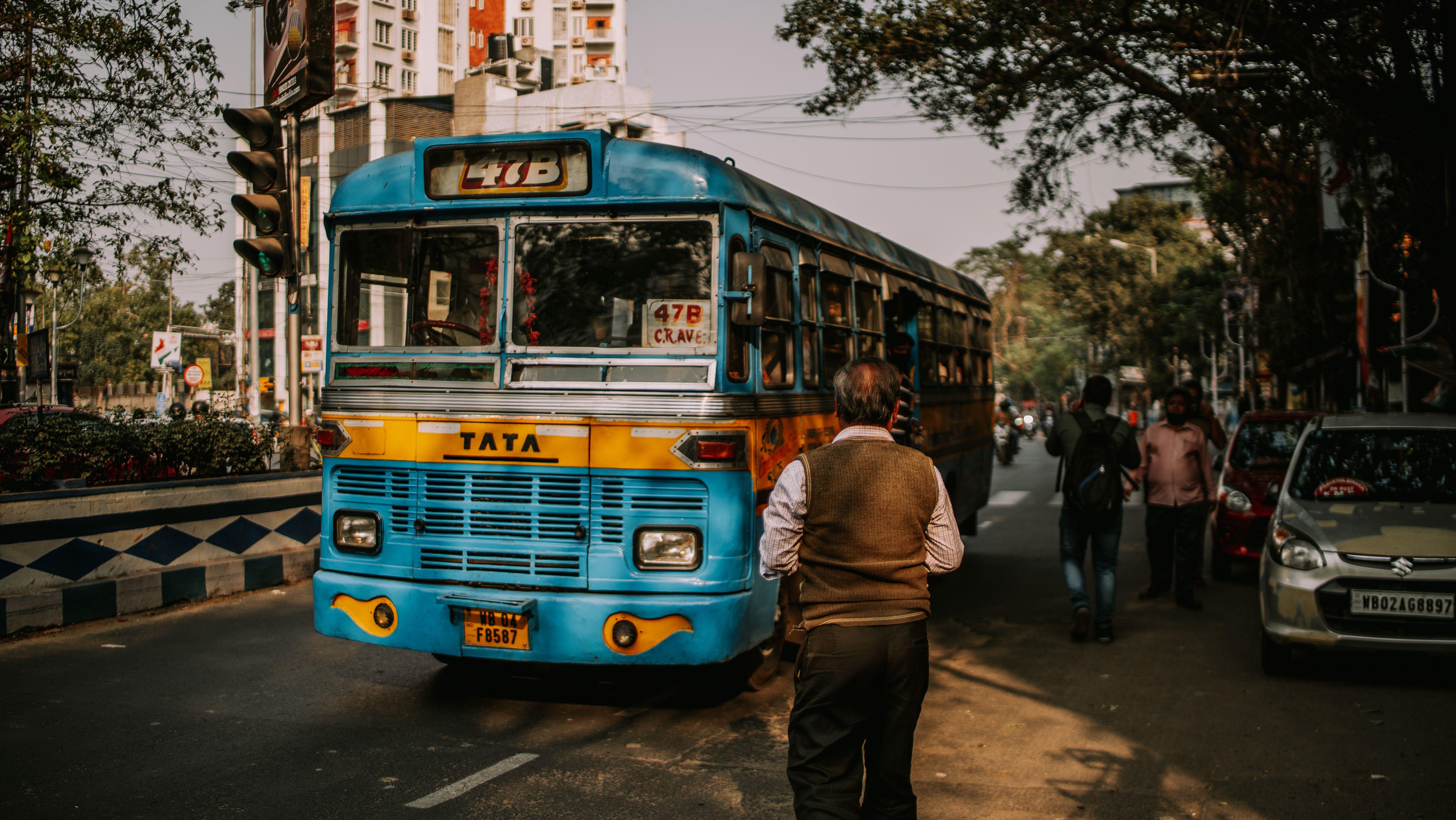 A blue bus in an urban environment with pedestrians and traffic on a city street.
