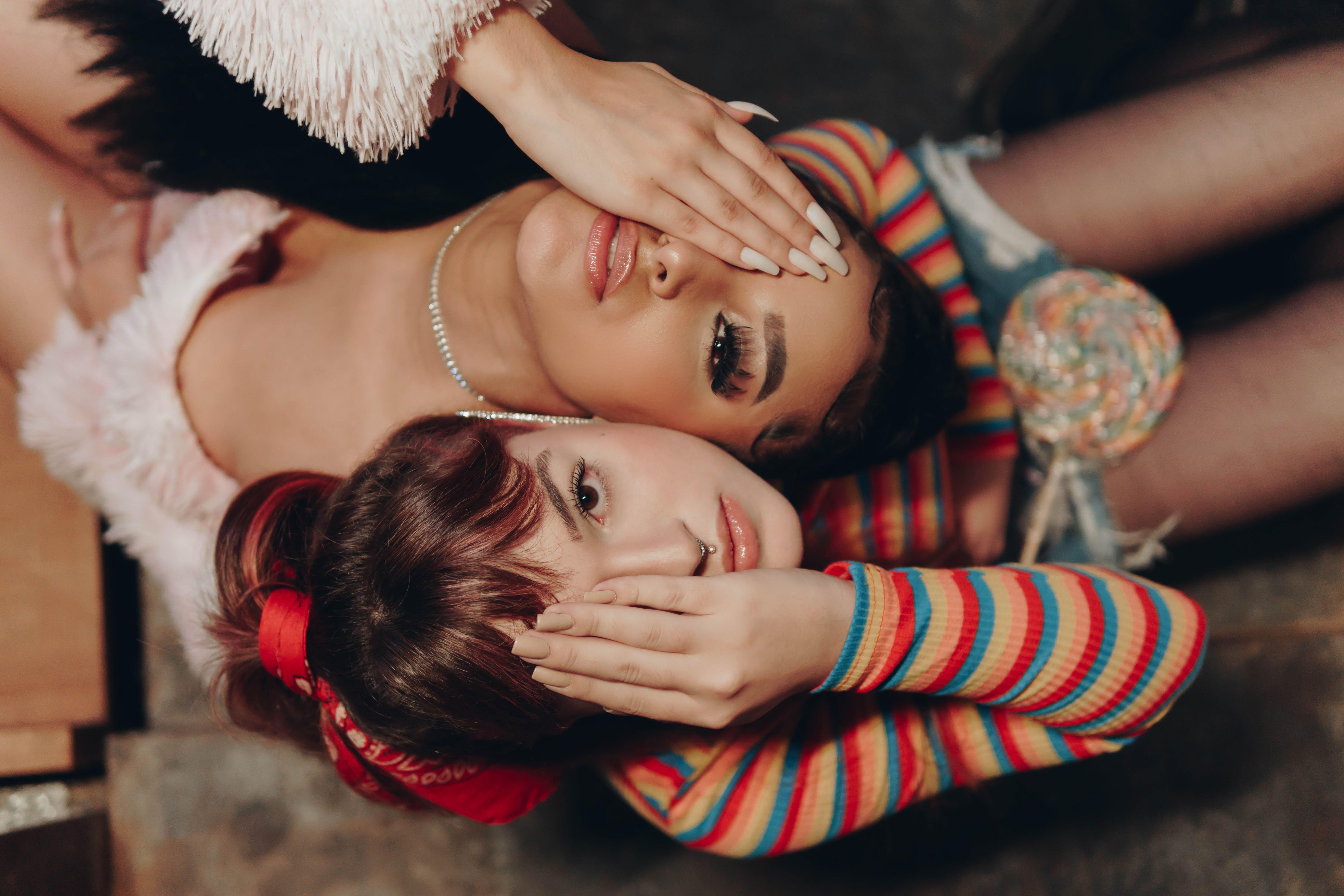 Two fashionable women lying down with playful poses, expressing youthful vibes and modern style indoors.