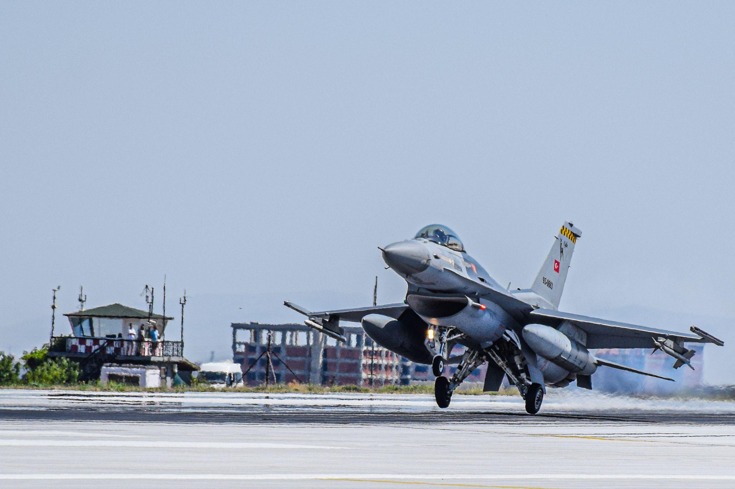 A military fighter jet taking off from an airport runway under a clear blue sky.