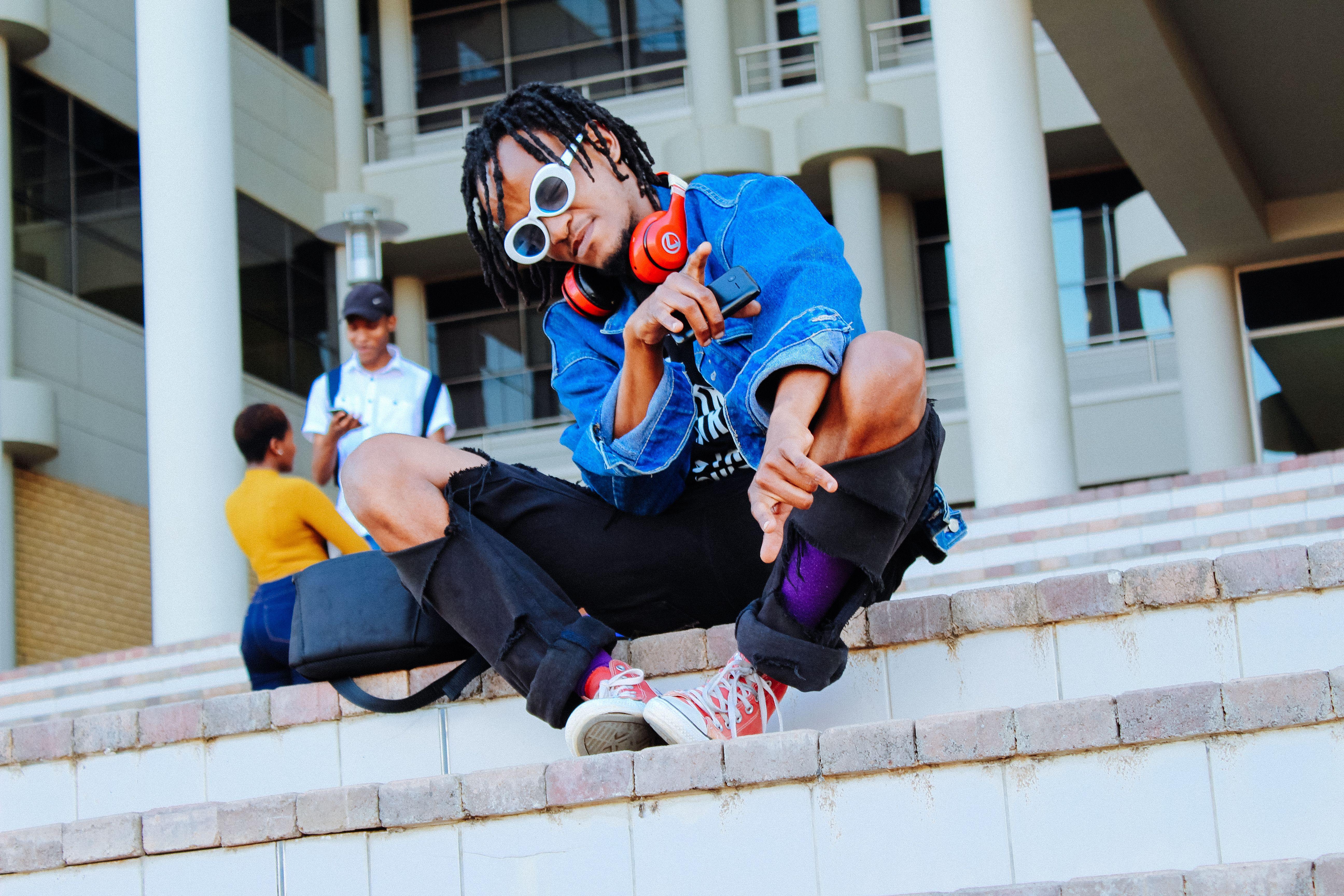 Stylish young adult sitting on urban stairs wearing headphones and sunglasses in Gaborone.
