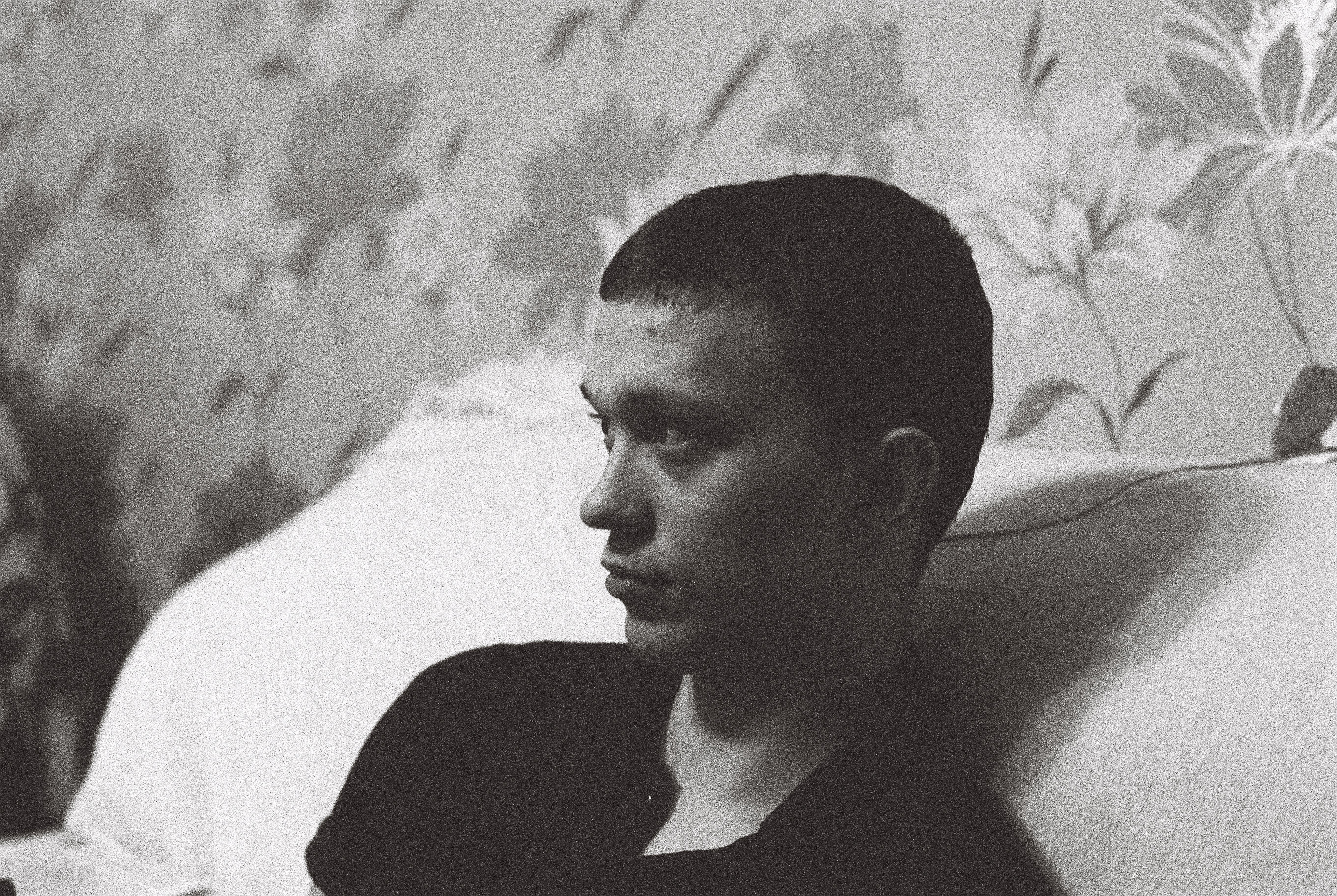 A man leans on a sofa, deep in thought, captured in striking black and white.