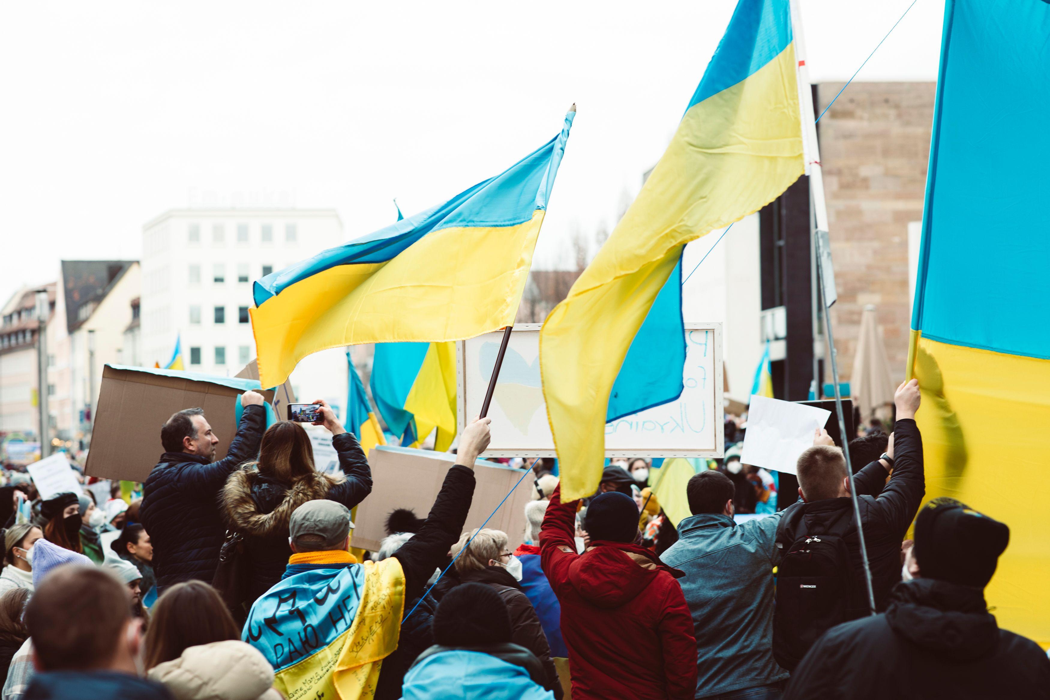 Crowd holding Ukrainian flags during a peaceful protest in urban setting.