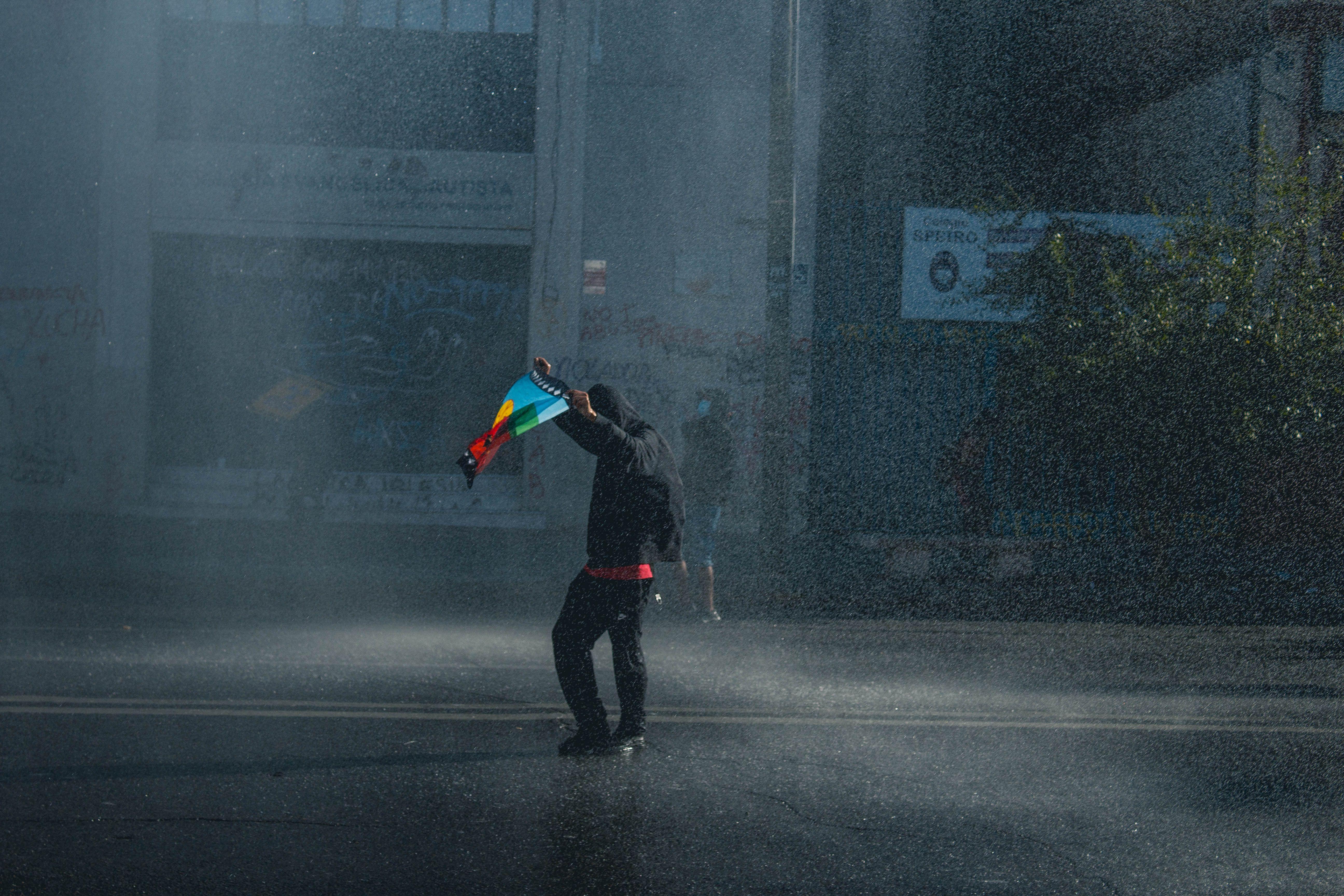 A lone protester holding a flag on a rainy street, symbolizing activism and resilience in Valparaíso, Chile.