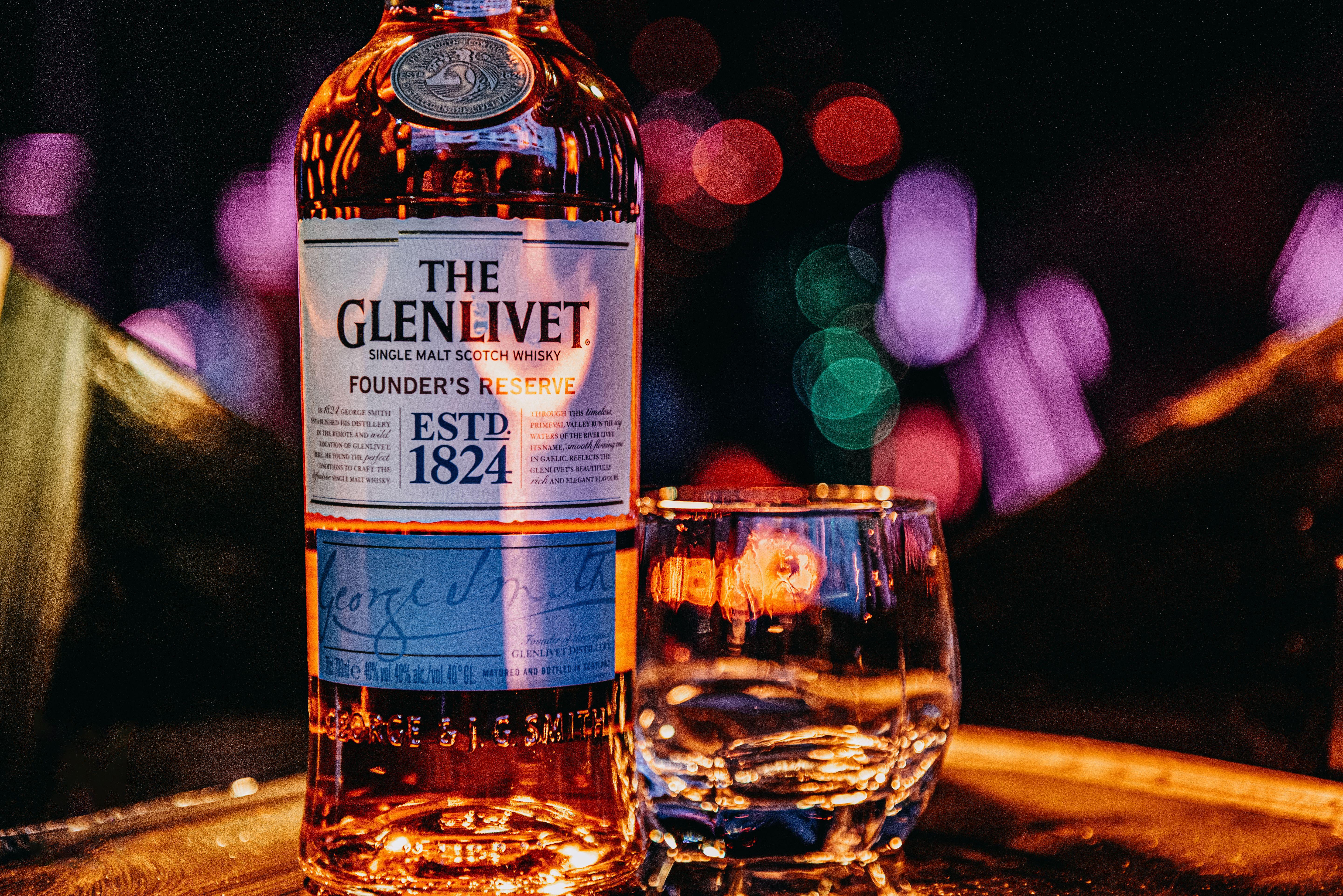 A Glenlivet bottle and glass on a tray with colorful bokeh lights in the background.