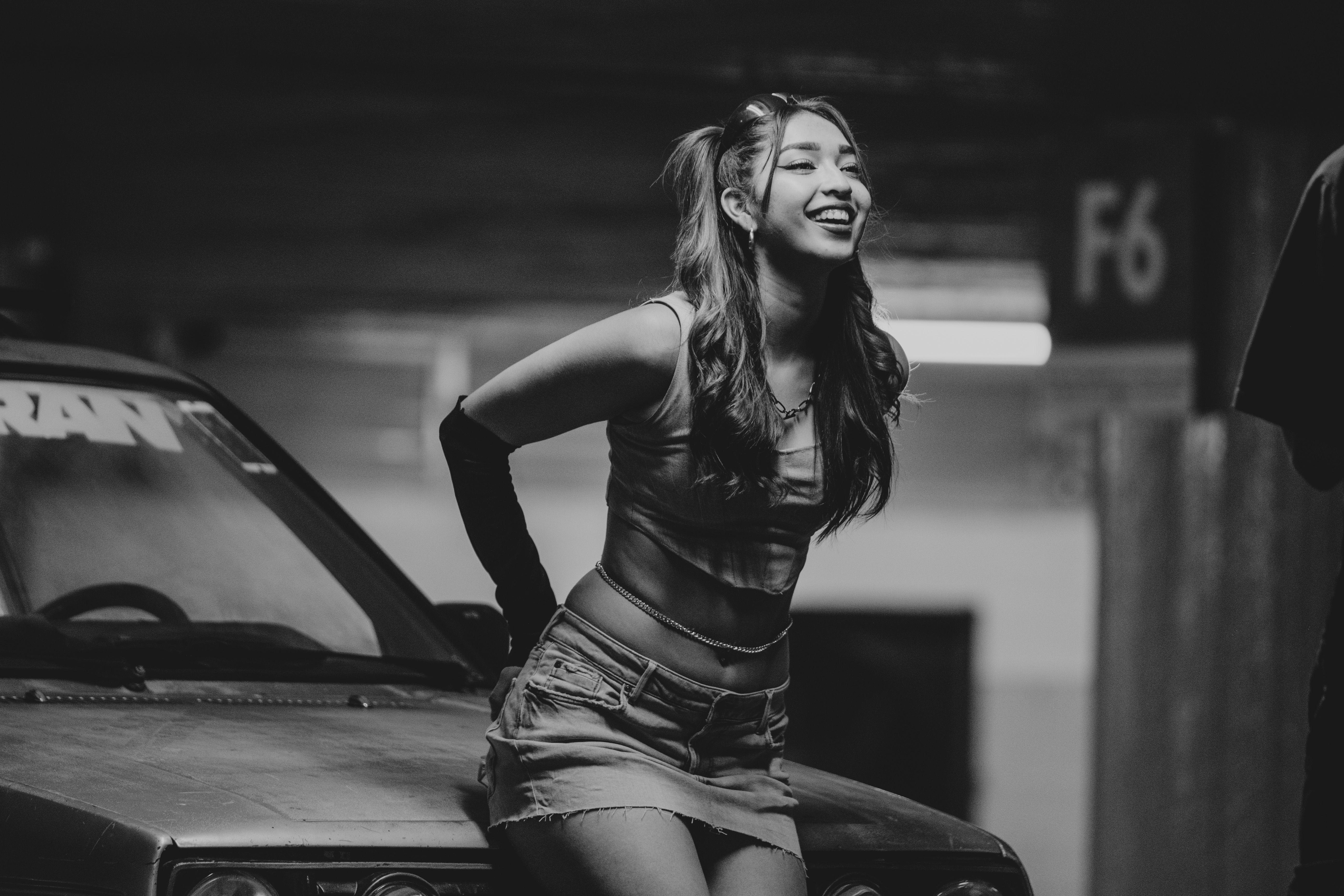 Smiling woman leaning on car in parking garage, black and white photo.