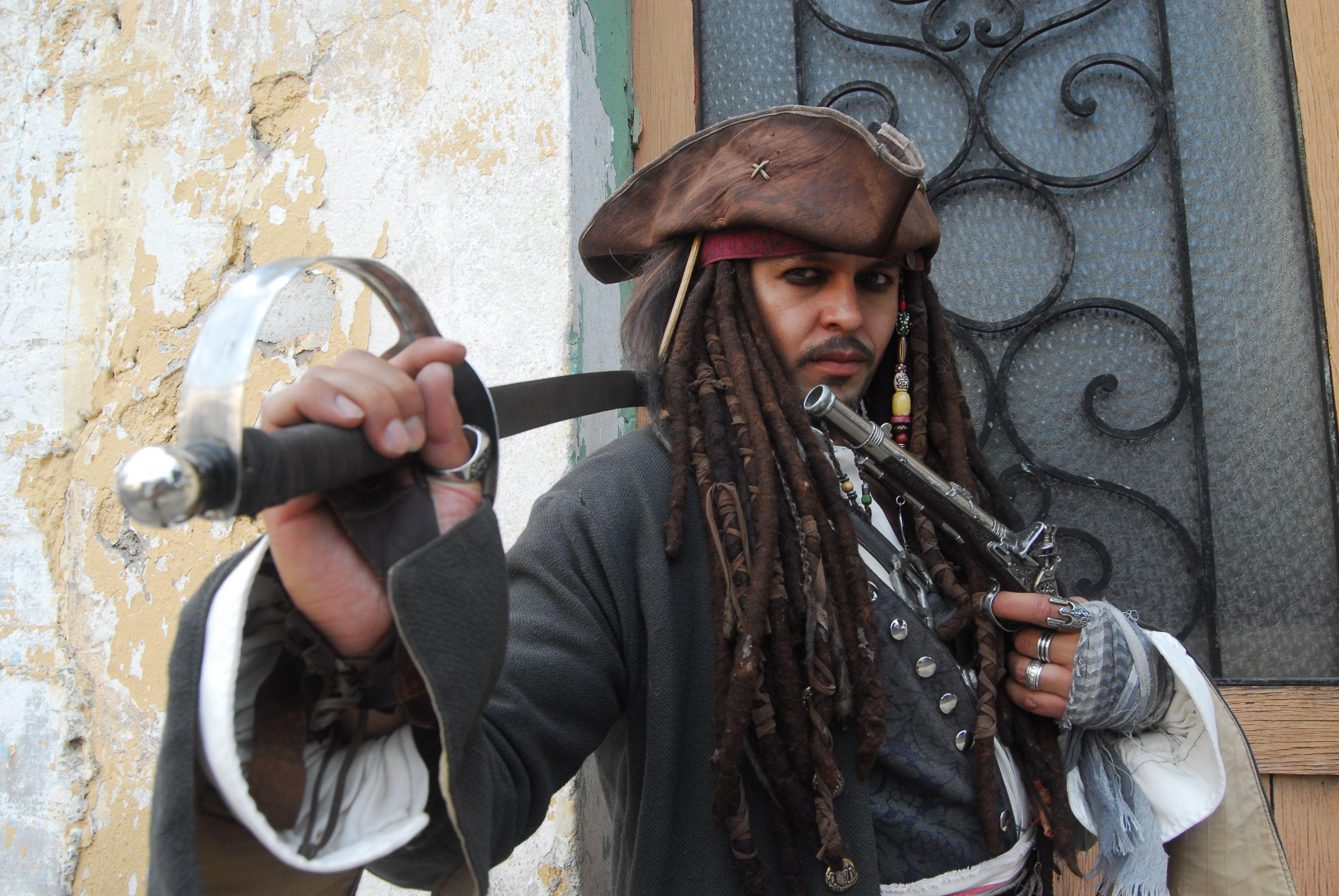Pirate cosplay enthusiast poses with sword and hat at indoor location.