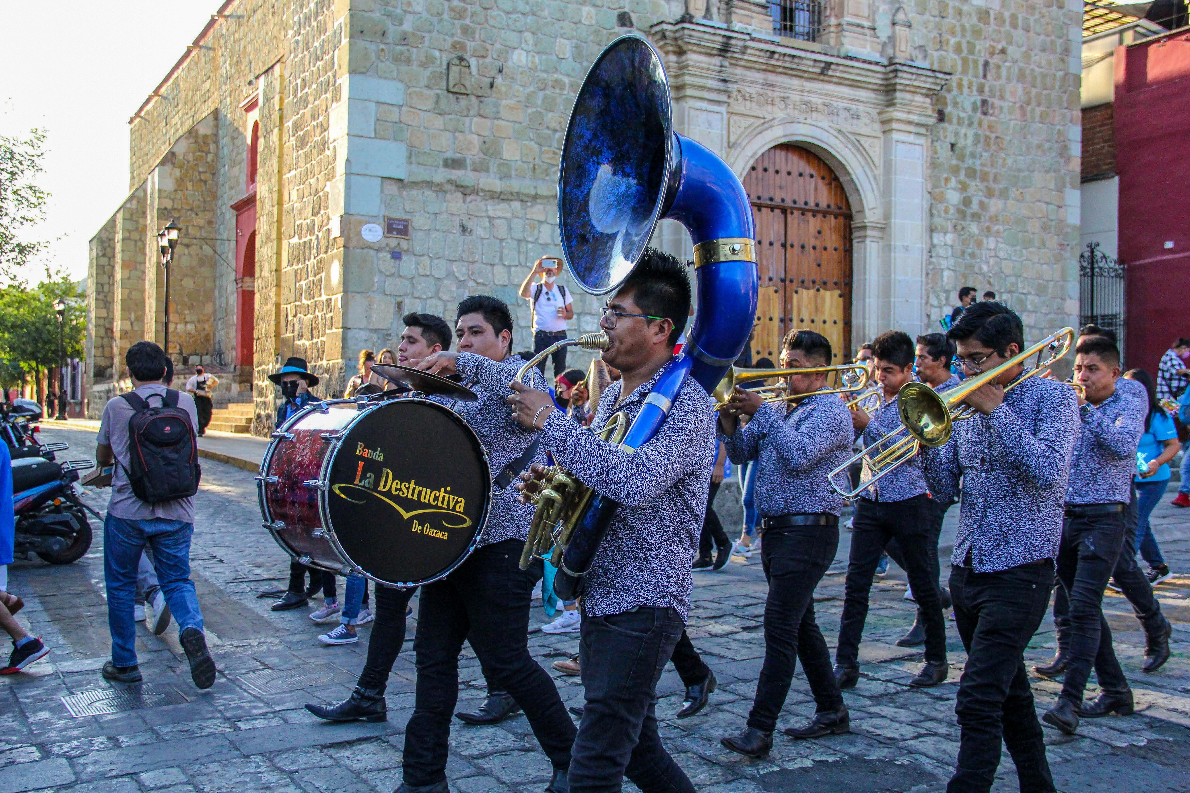 Vibrant brass band marches through historic Oaxaca street during a lively parade.