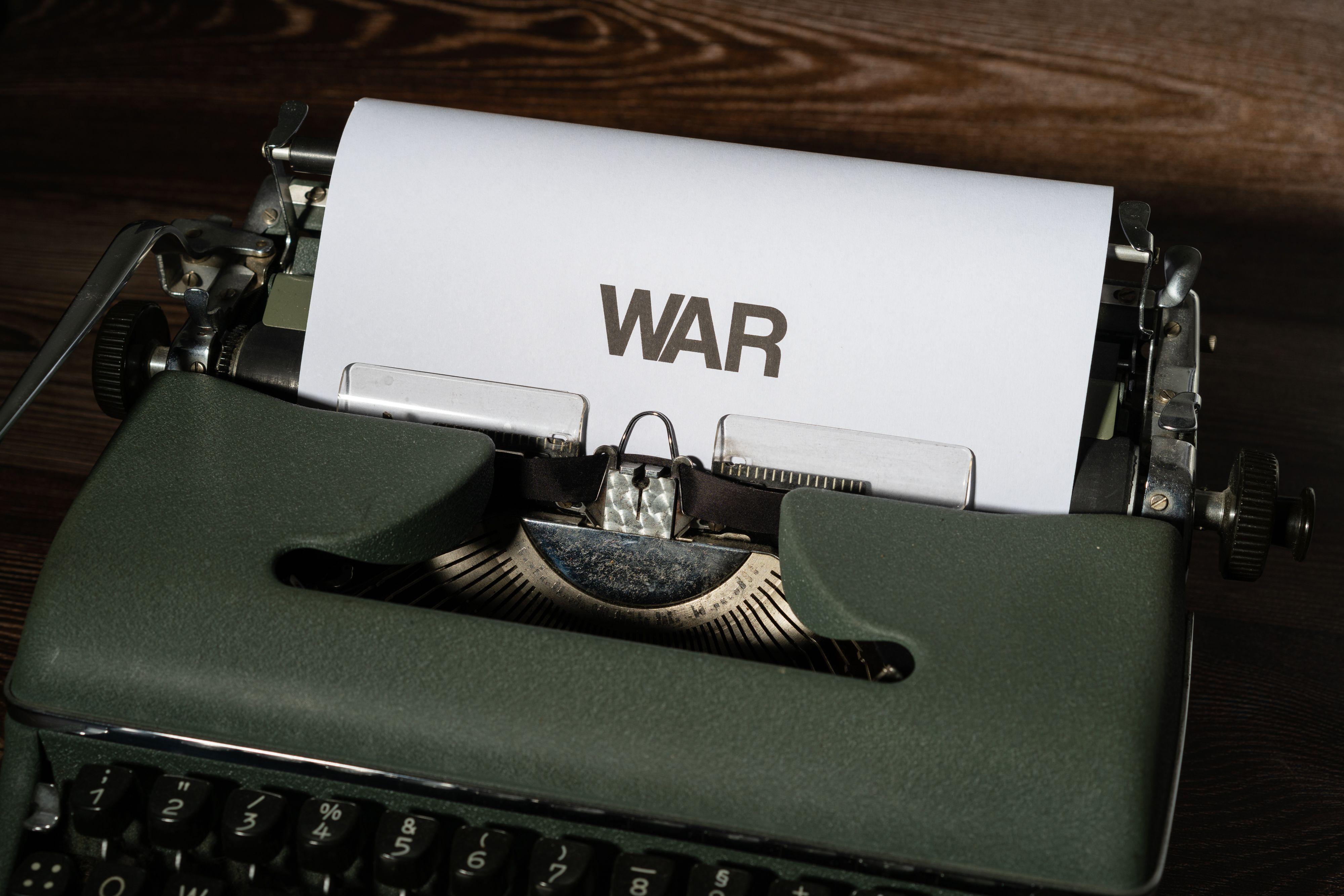 Close-up of an antique typewriter with the word 'WAR' typed on paper, on a wooden surface.
