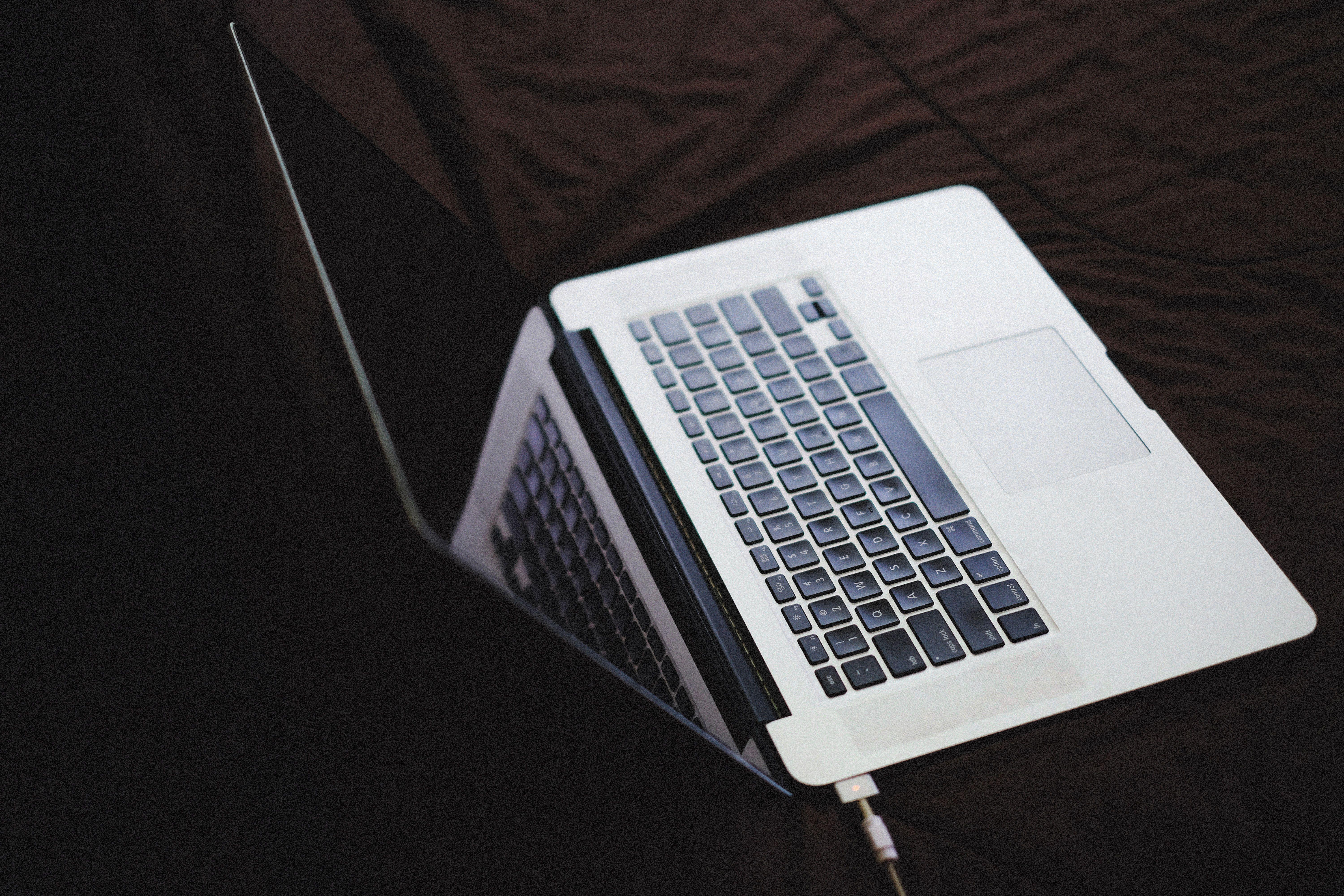 Modern laptop with backlit keyboard on a dark fabric surface, connected to a charger.