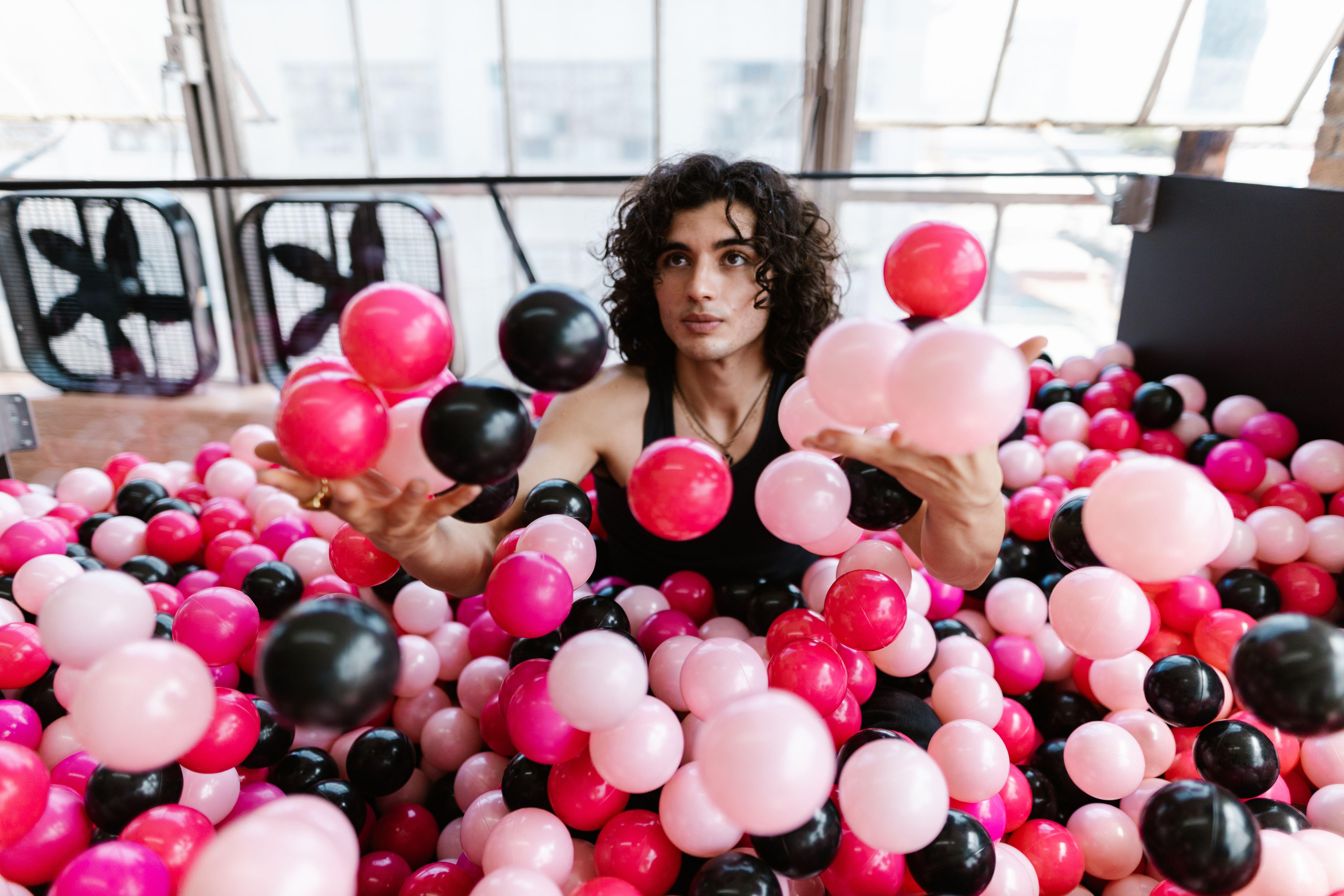 A young man plays joyfully in an indoor ball pit filled with vibrant balls.