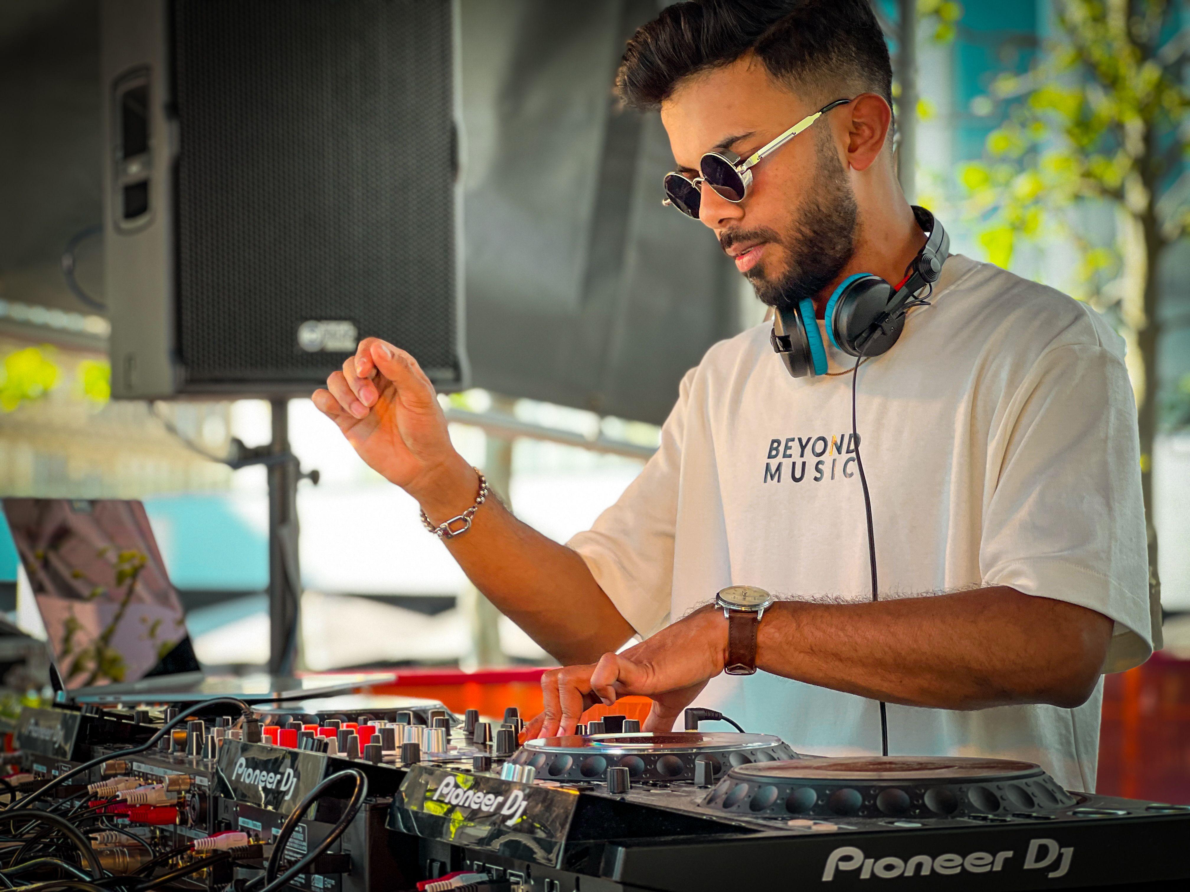 A stylish DJ wearing sunglasses and headphones mixes tracks outdoors using a turntable.