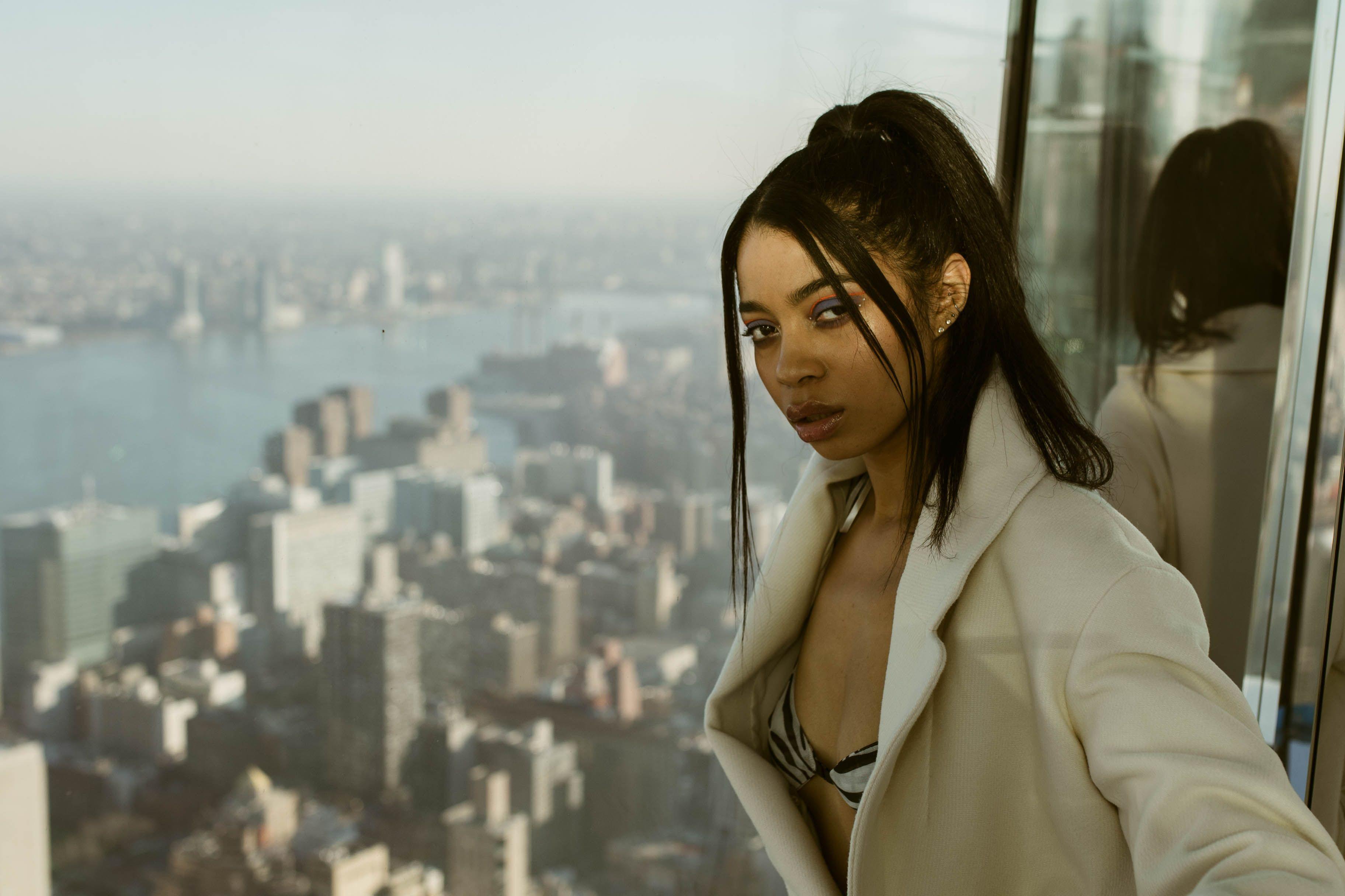 Stylish woman posing on an observation deck with a panoramic NYC skyline view.