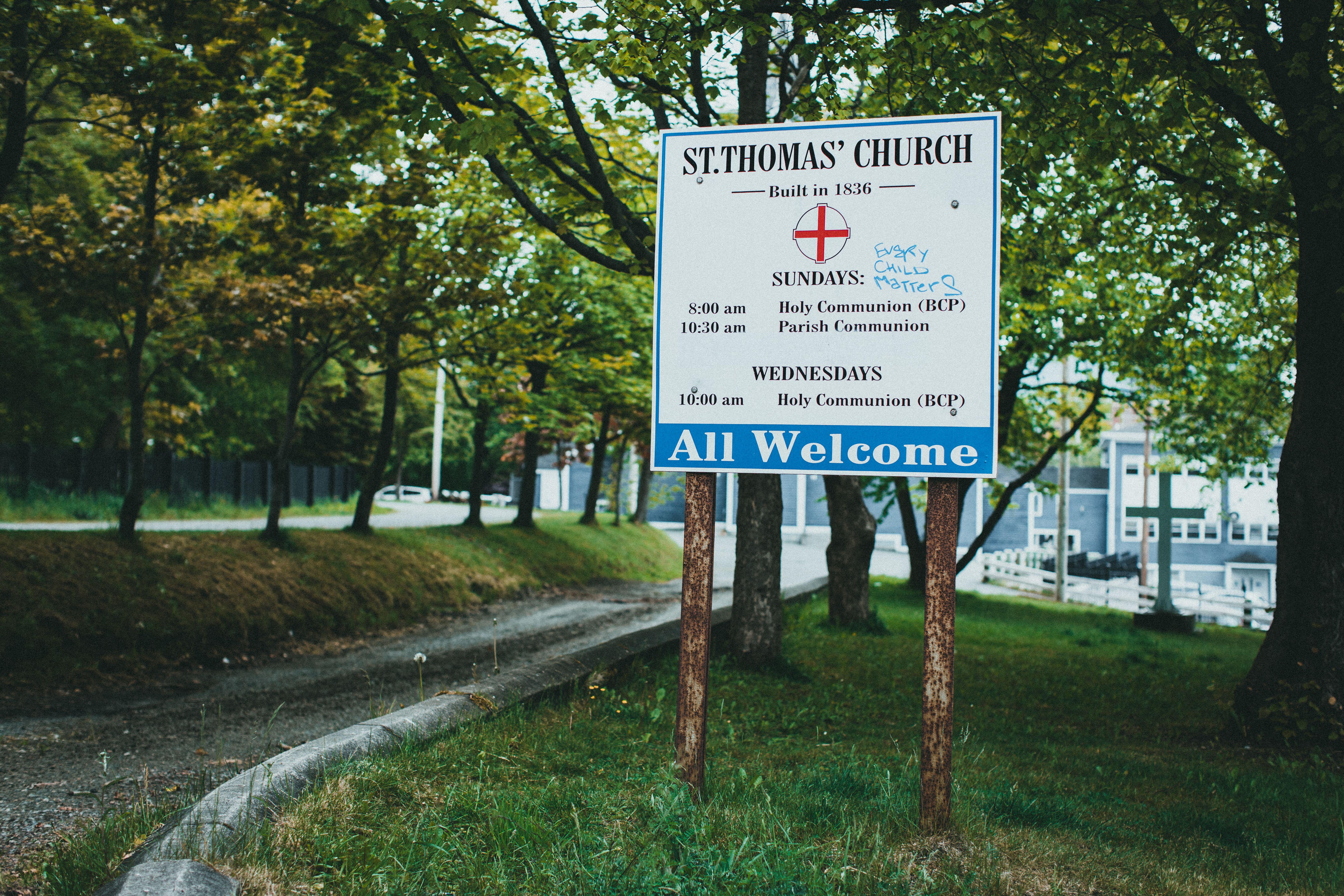 Welcome sign outside St. Thomas' Church surrounded by lush greenery and trees.
