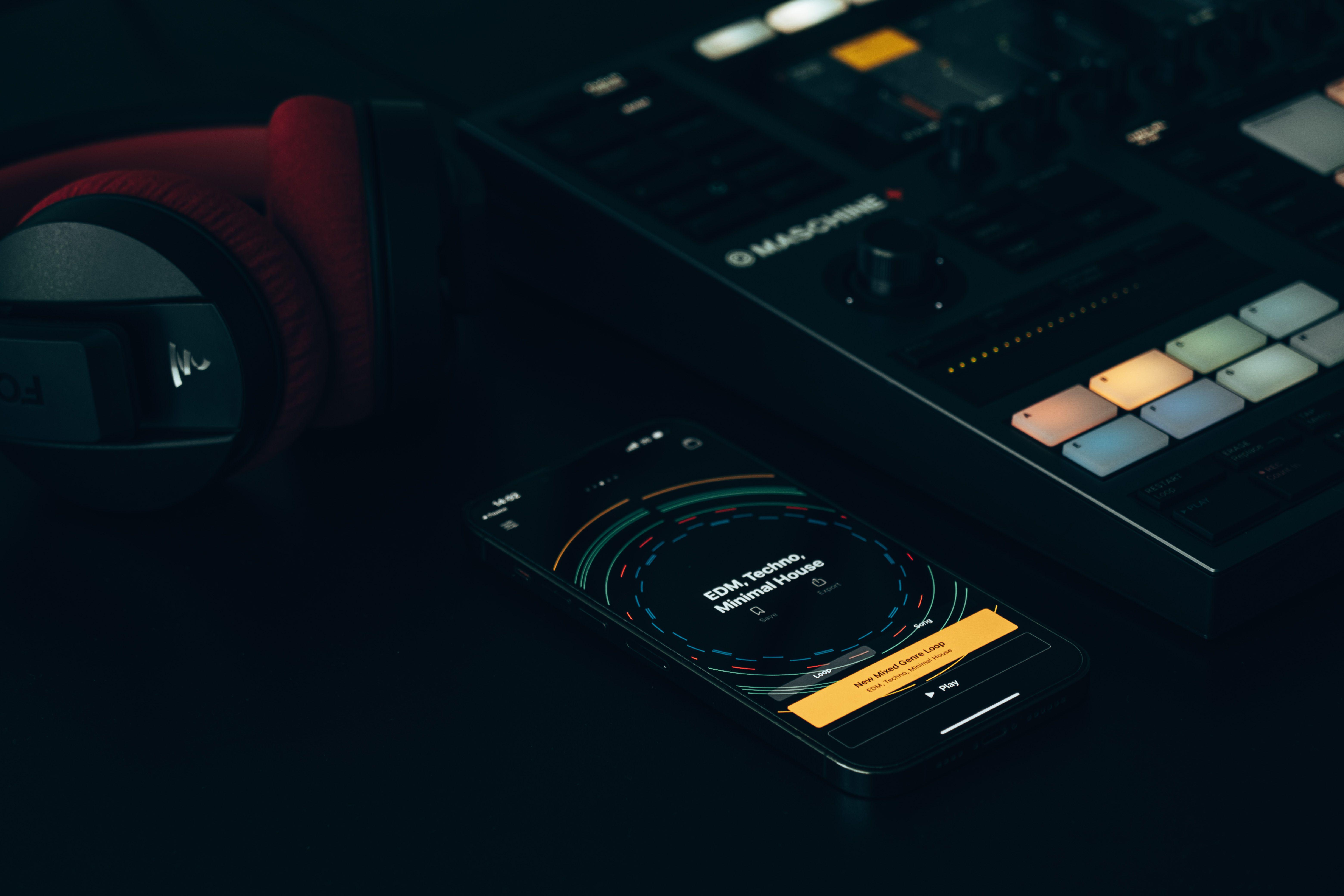 Dark-themed music setup featuring a DJ controller, smartphone, and headphones on a sleek surface.
