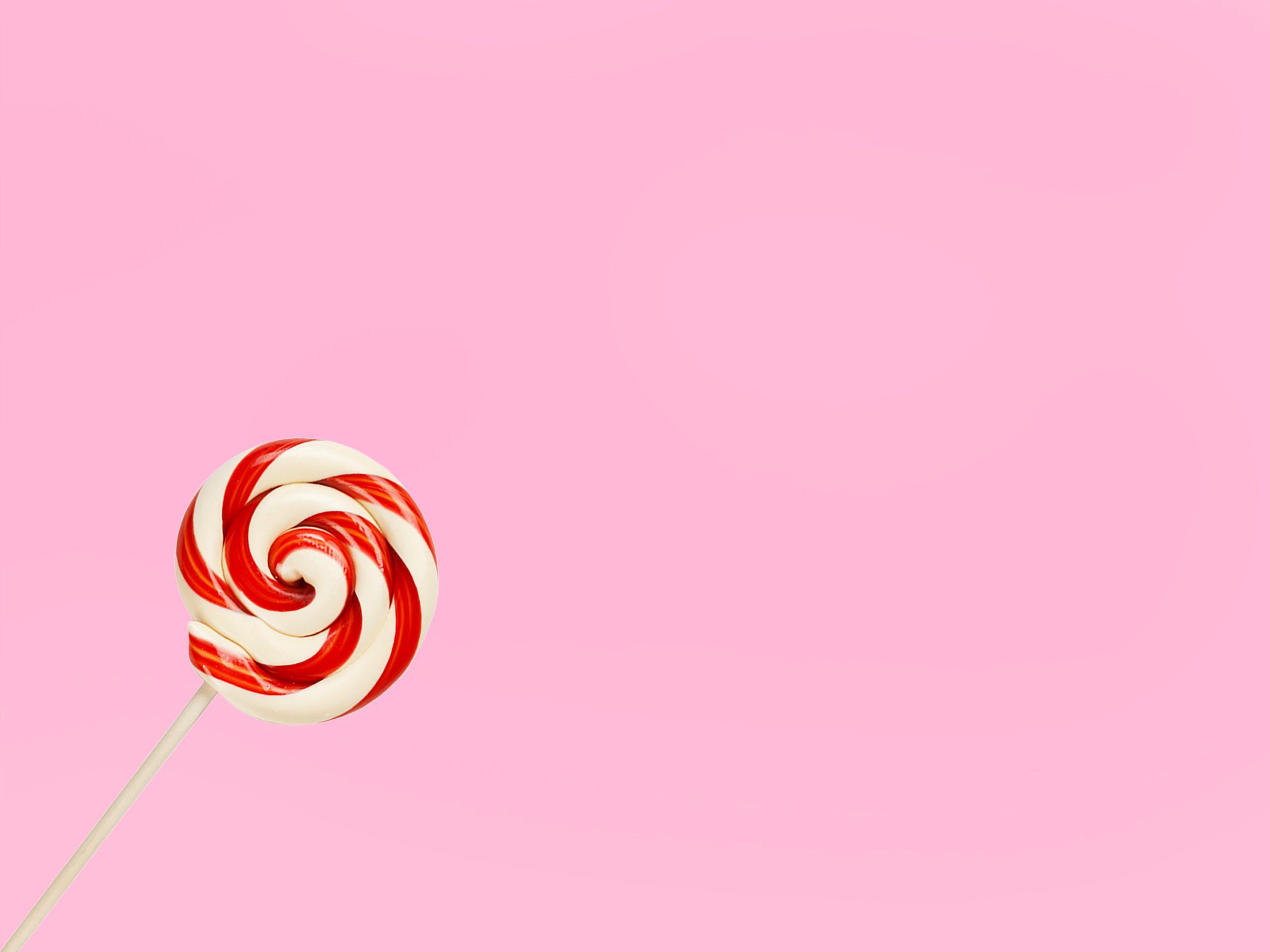 Vibrant red and white lollipop on a pastel pink background, perfect for confectionery themes.