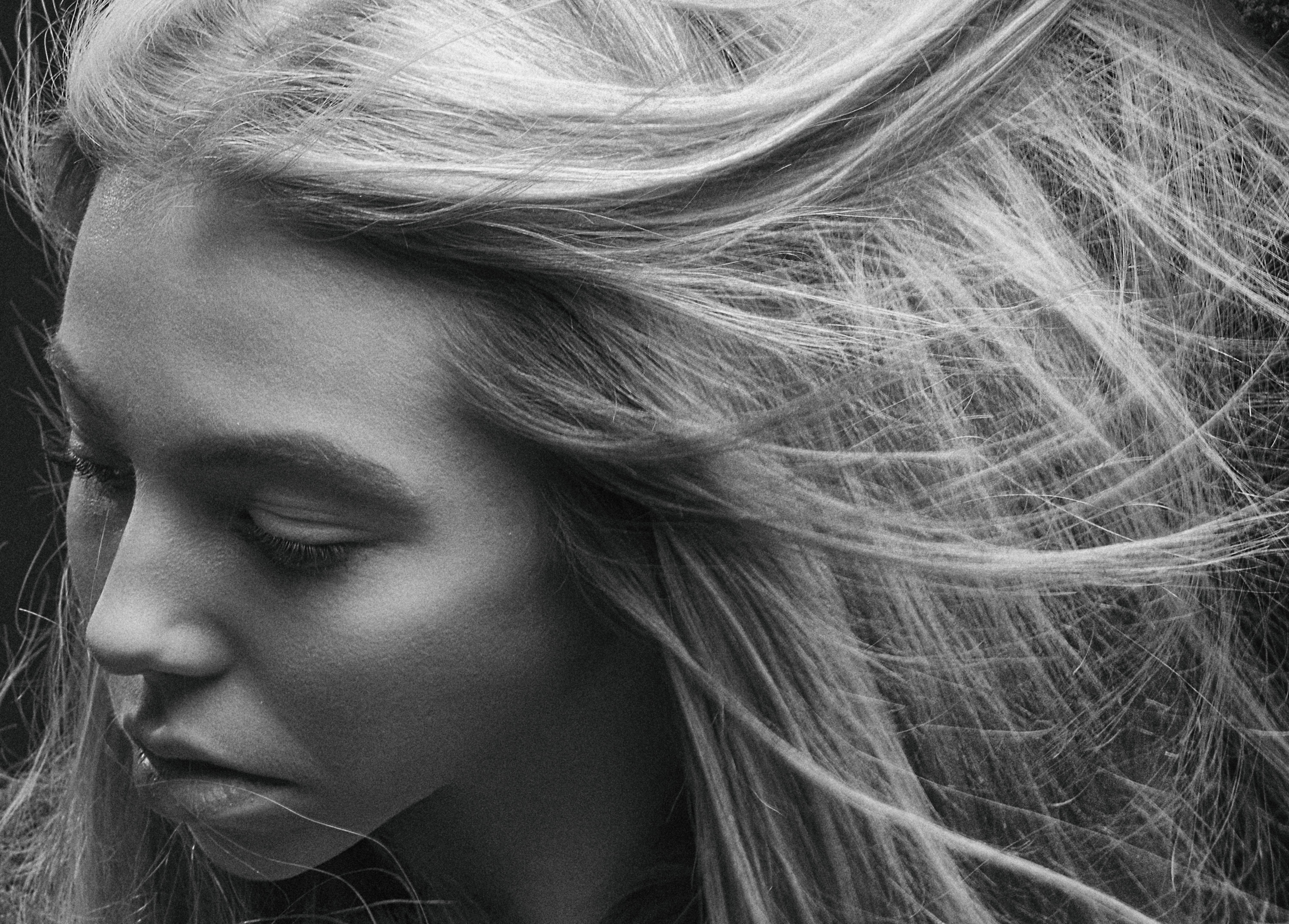 Black and white close-up portrait of a woman with wind-swept hair, capturing emotion and movement.