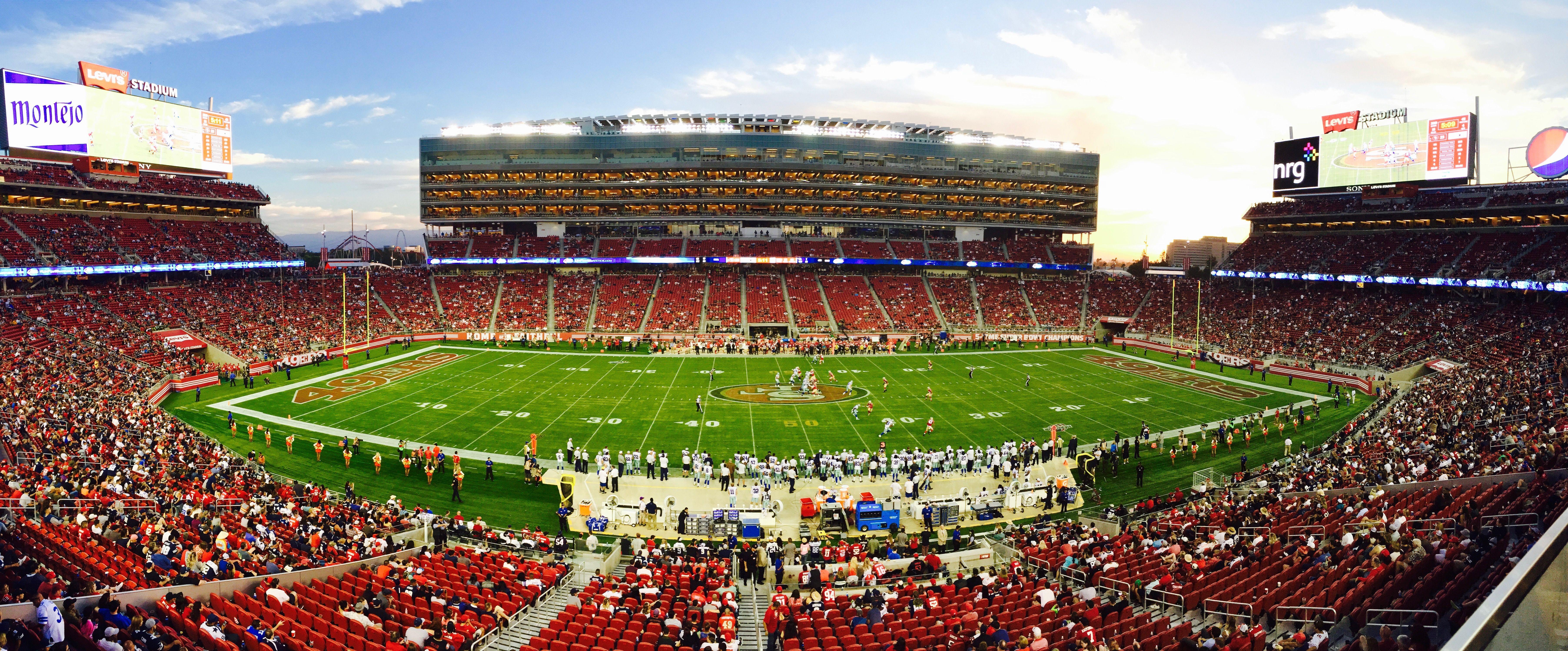 A stunning panoramic shot of Levi's Stadium in Santa Clara during a packed football game at sunset.