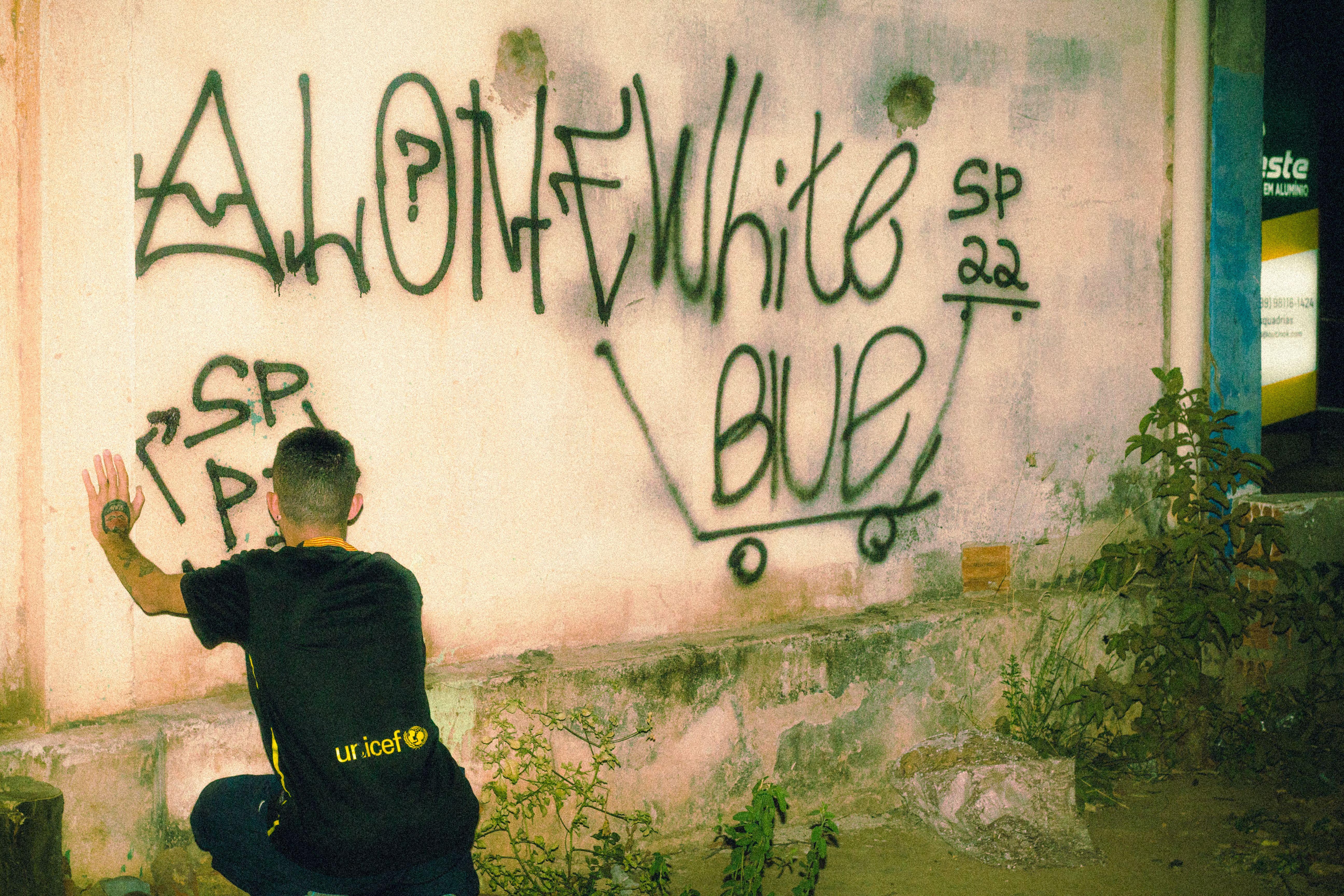 A young man sits in front of a graffiti-covered wall, embracing urban street art culture.