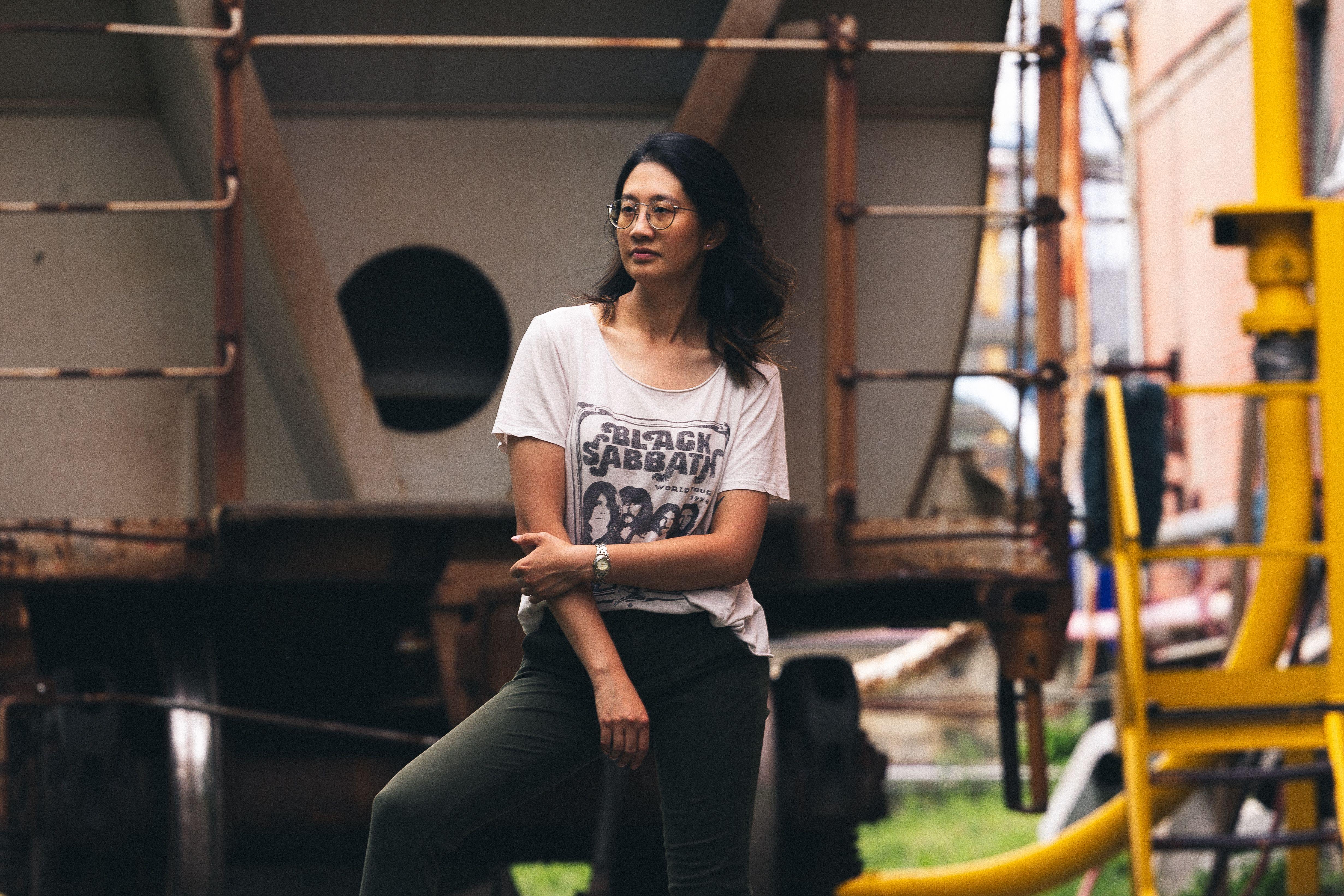 Asian woman in eyeglasses posing outdoors with industrial background.