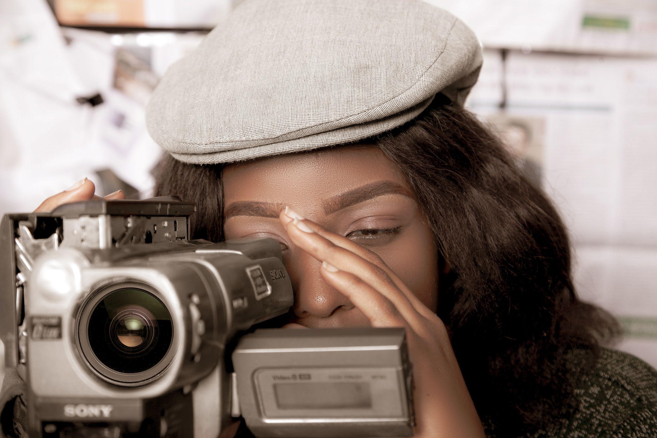 Black woman in vintage style filming with video camera, evoking a retro feel in Kampala.