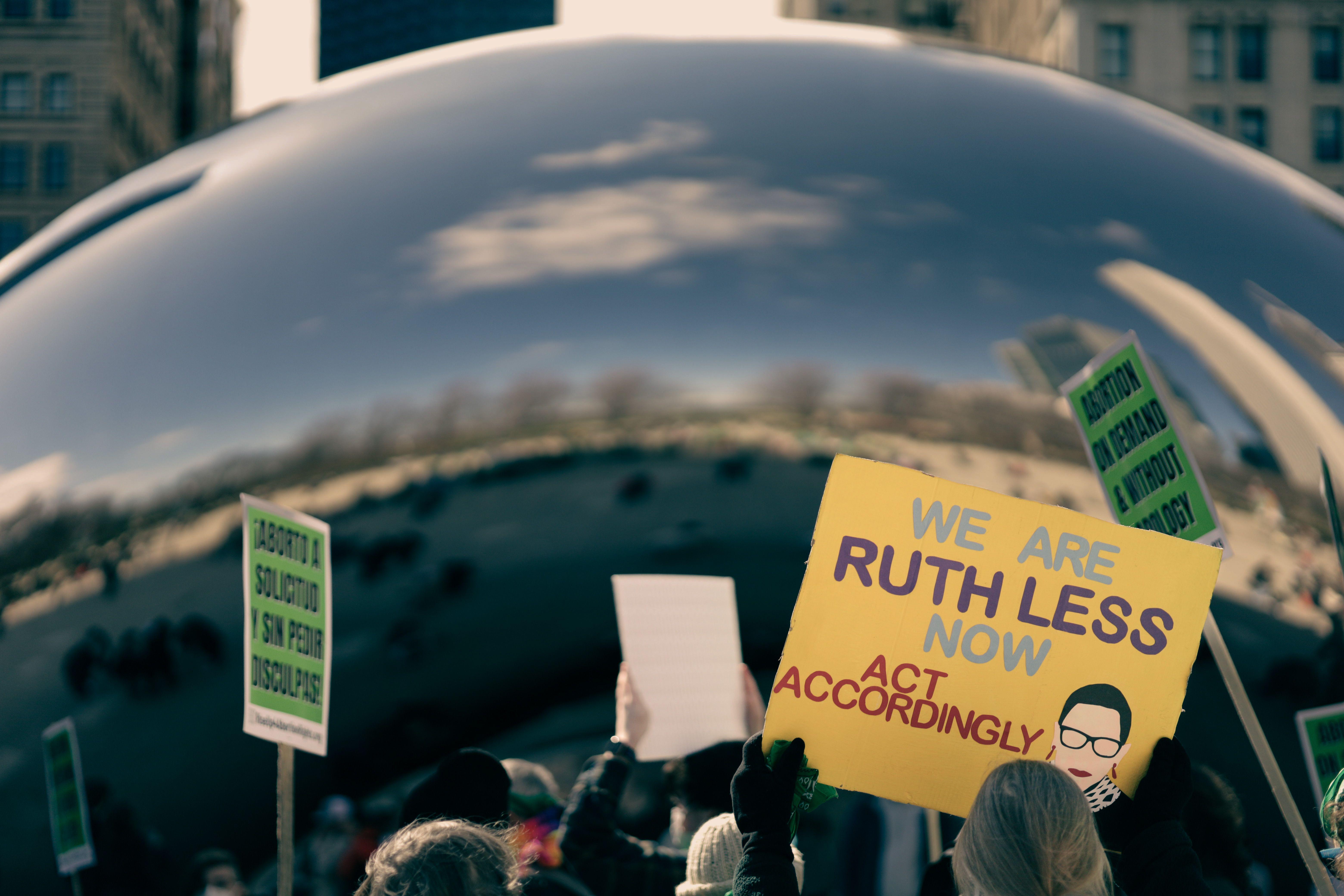 Crowd holding protest signs at Cloud Gate, Chicago, addressing abortion rights. Urban activism scene.