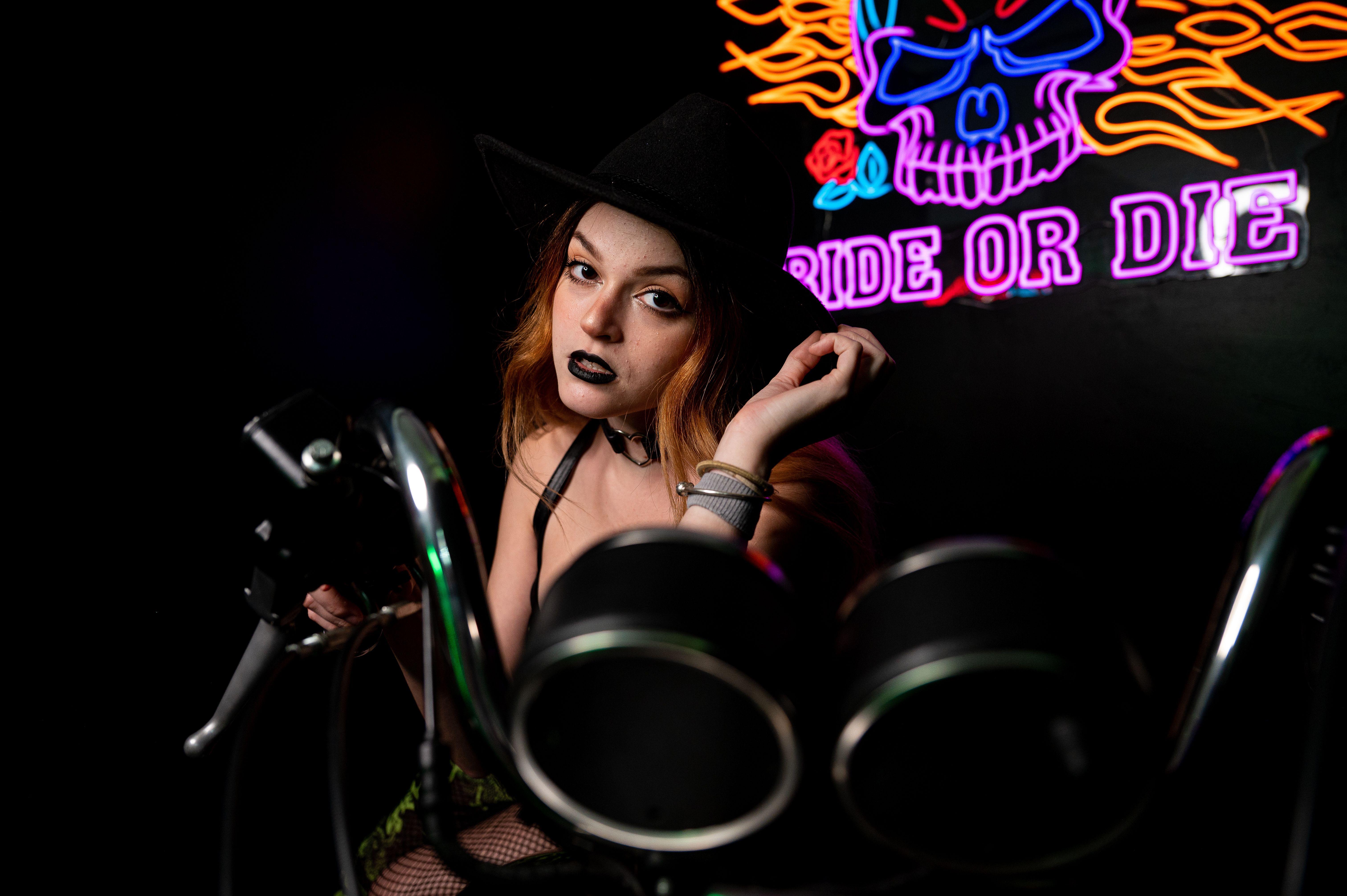Captured moment of a woman in dark makeup near a neon sign and motorcycle.