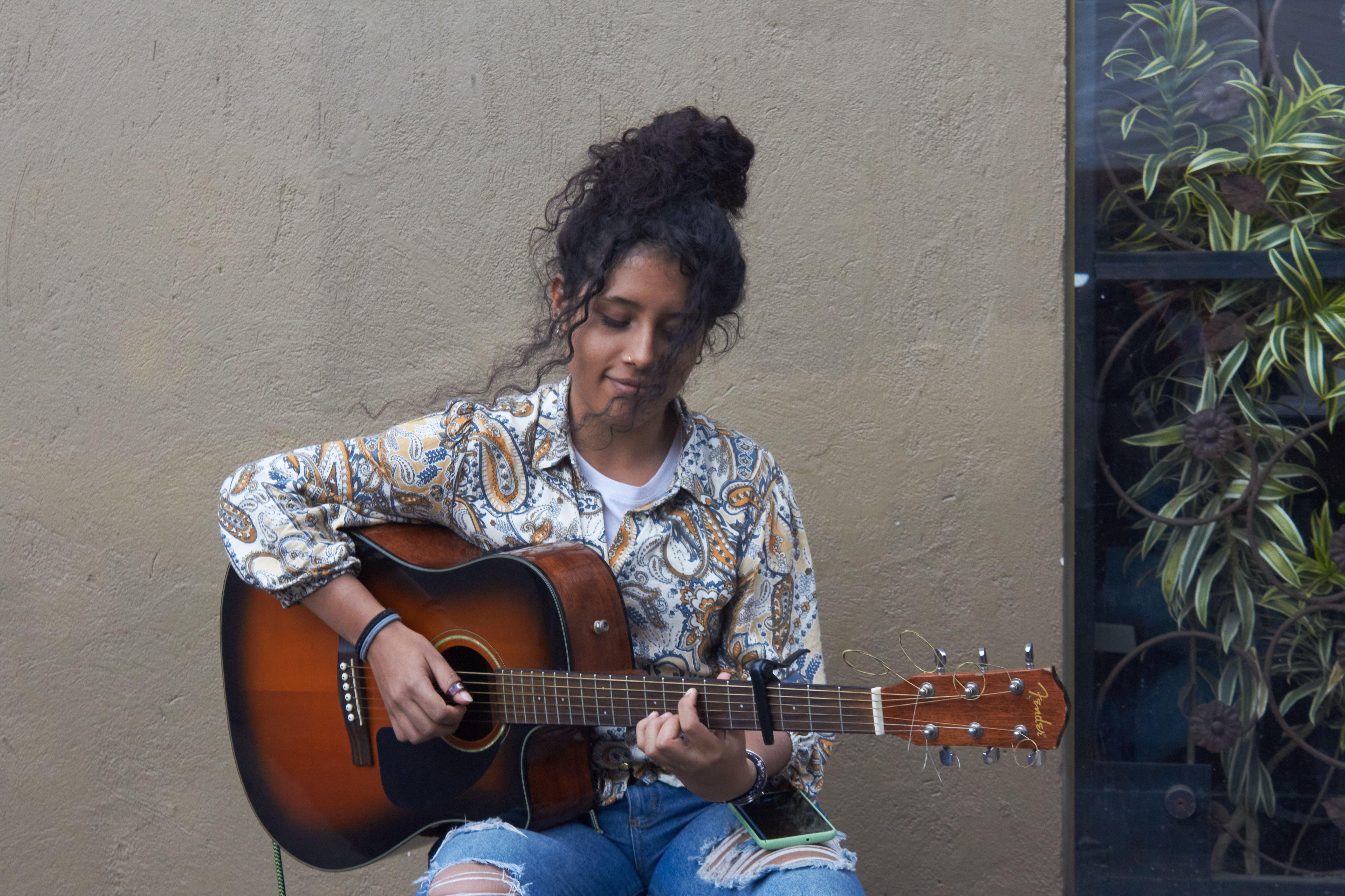 A young woman performs with an acoustic guitar against a textured wall in Bogotá.