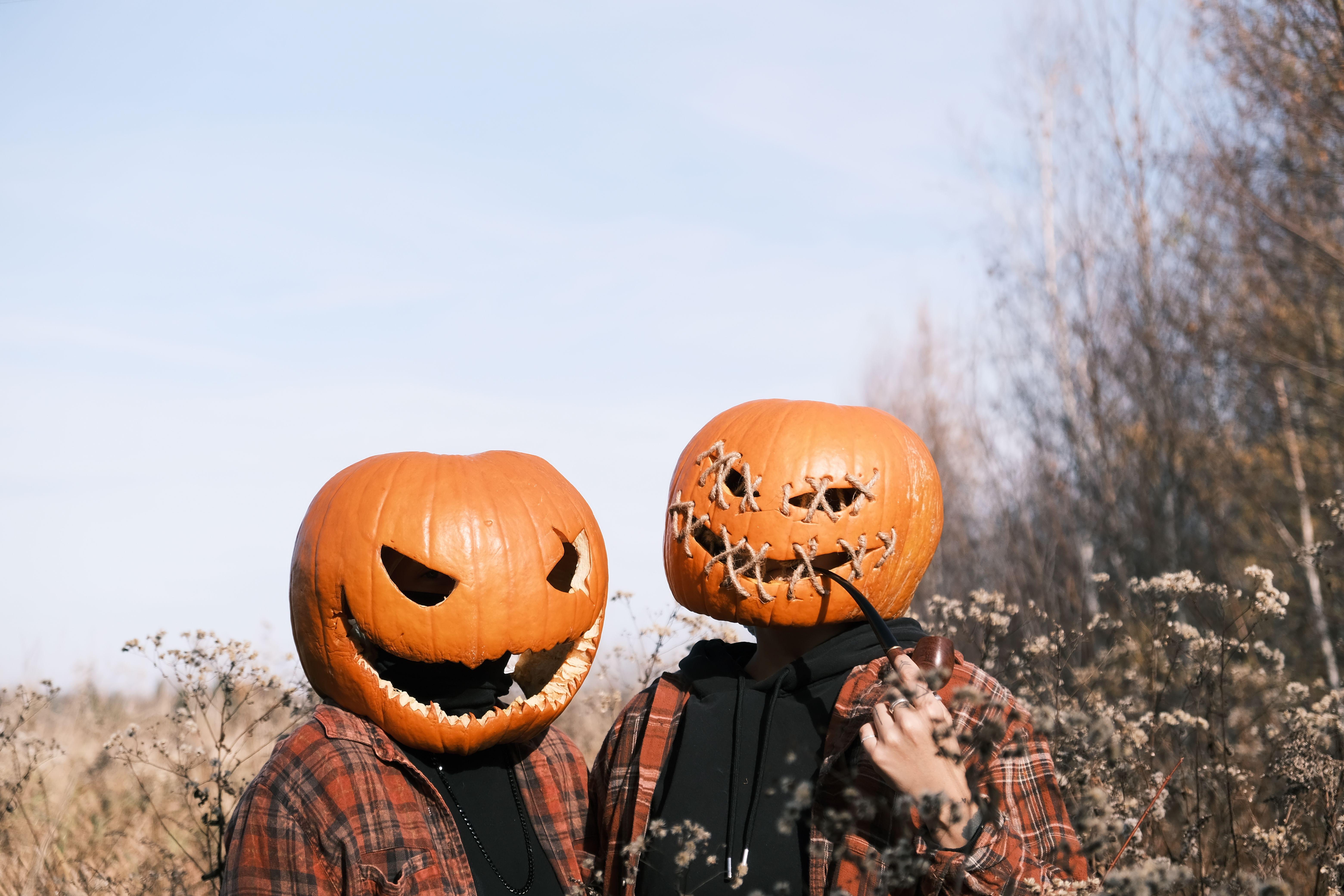 Two people wearing pumpkin heads in a field during fall, creating a spooky Halloween scene.