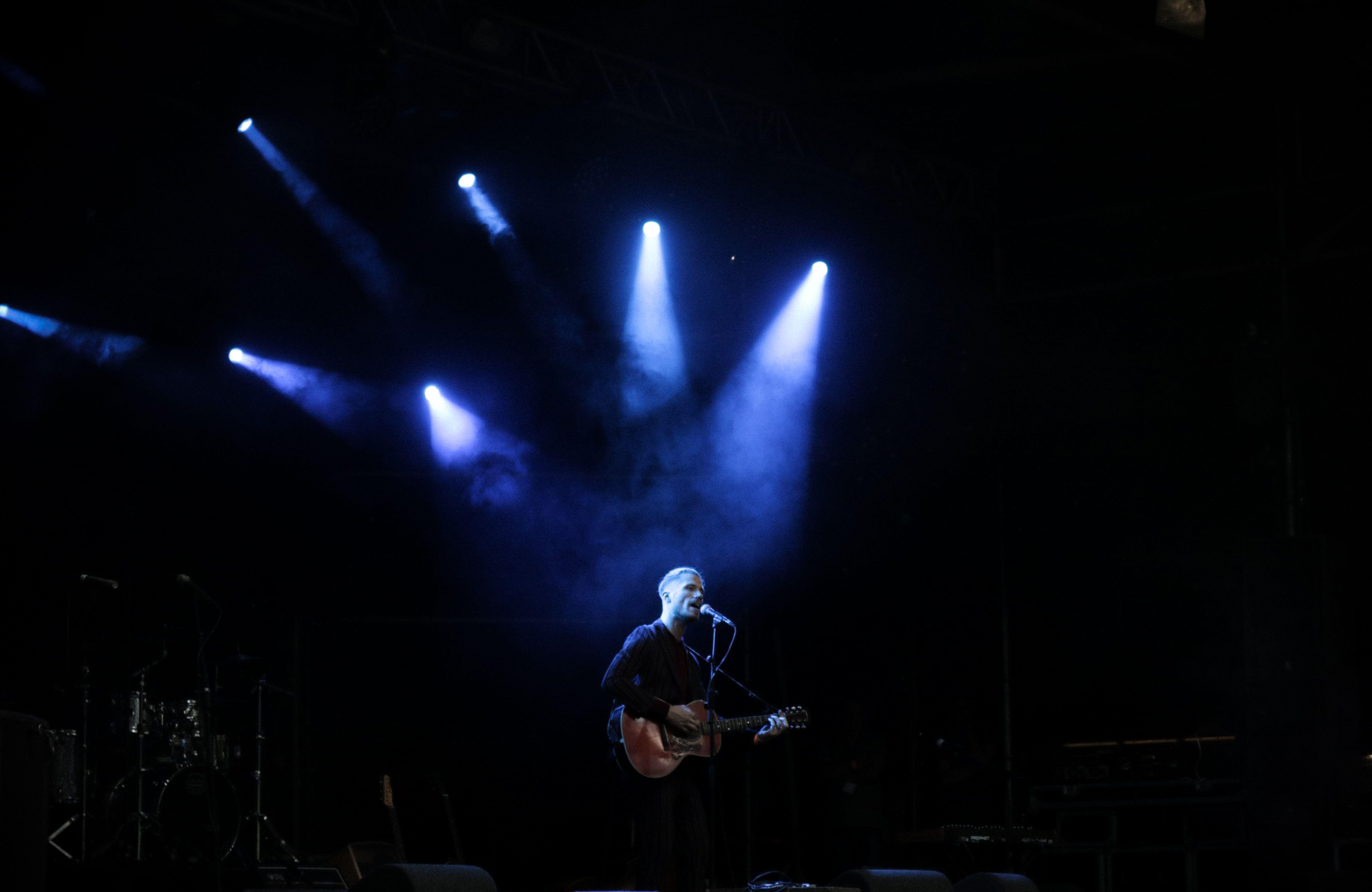Solo musician performs on stage with guitar under dramatic blue lighting during a live concert.