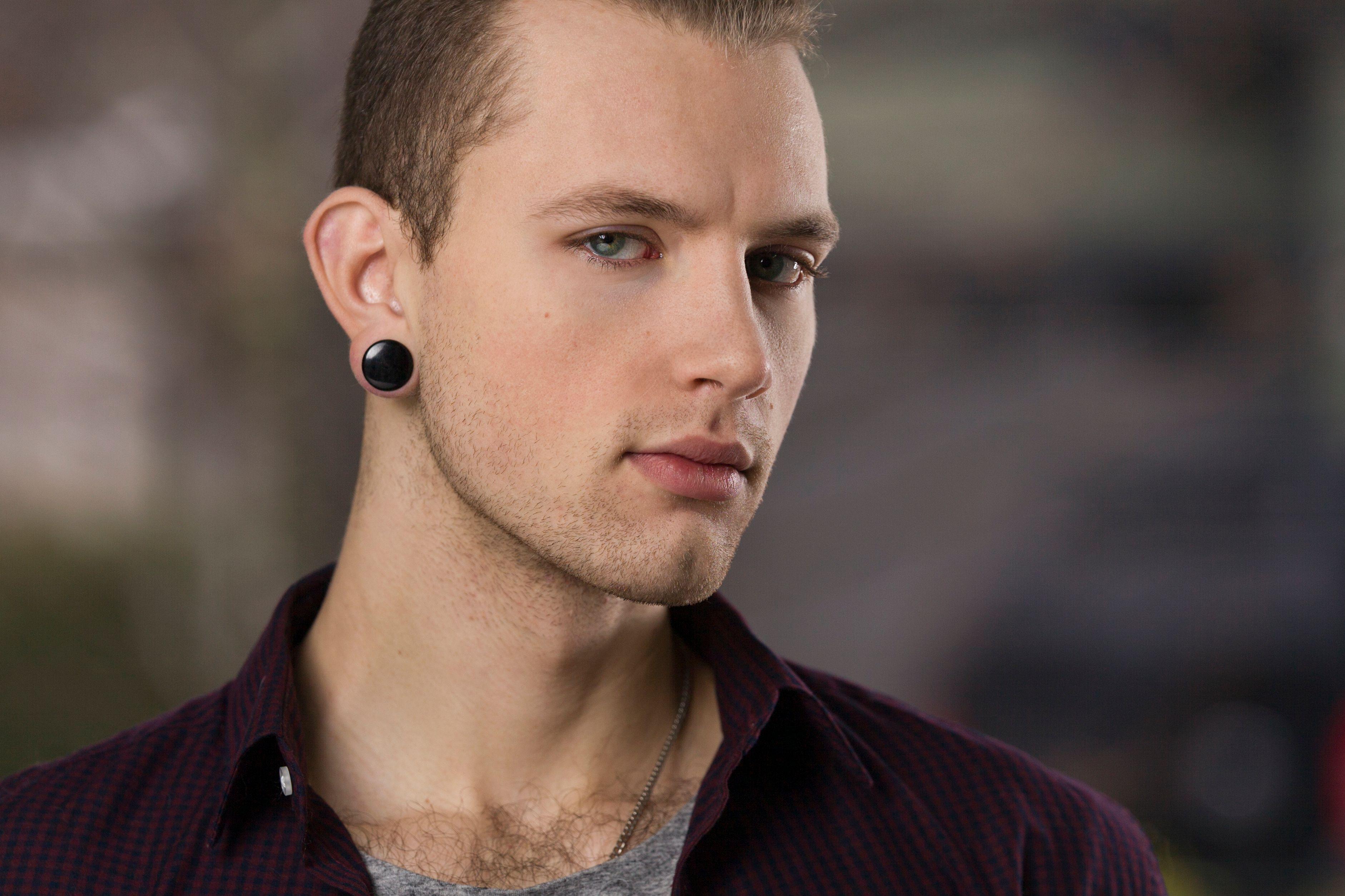 A portrait of a stylish man with earrings, exuding confidence and serious expression outdoors.