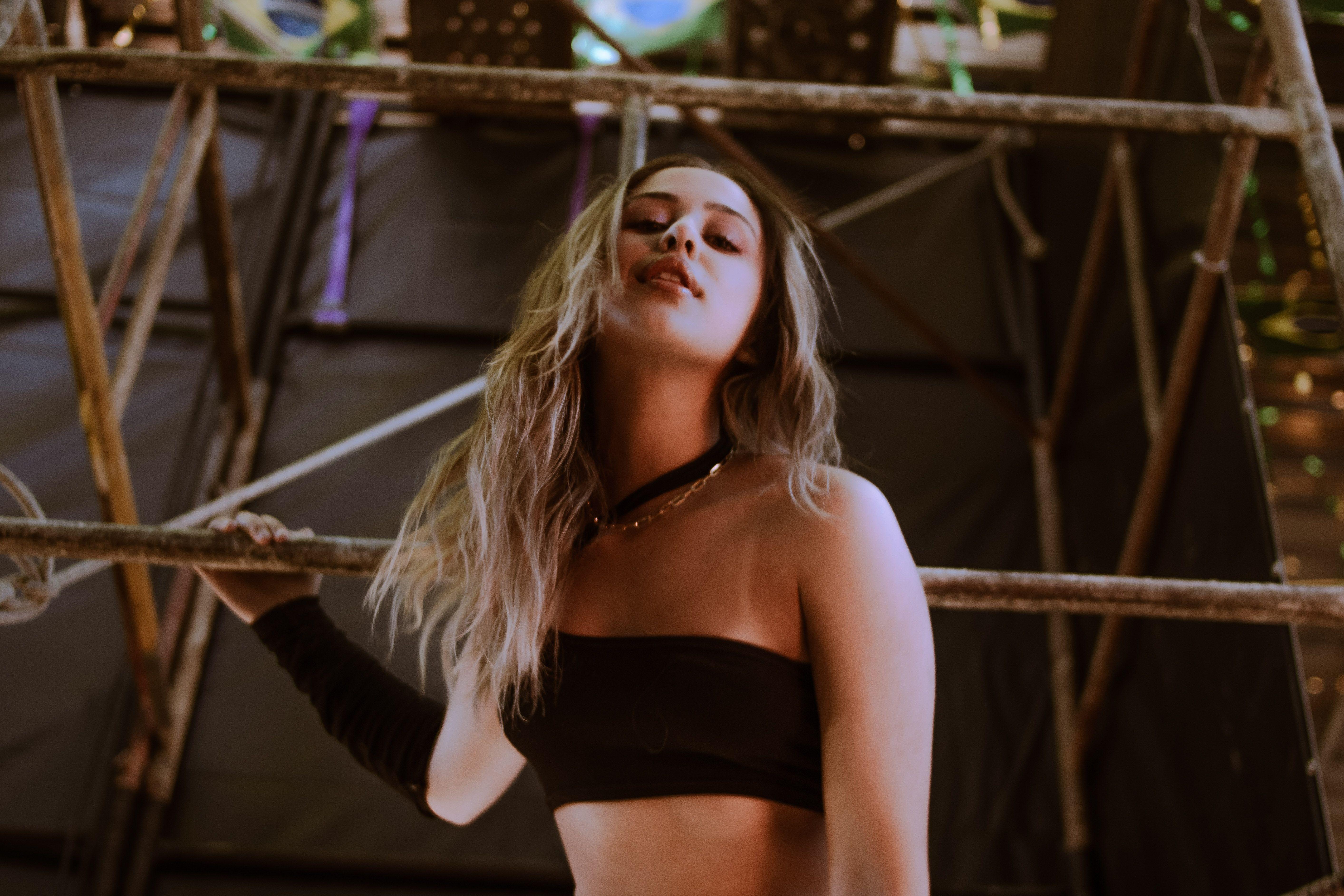 Stylish portrait of a blonde woman posing in a black tube top against scaffolding indoors.